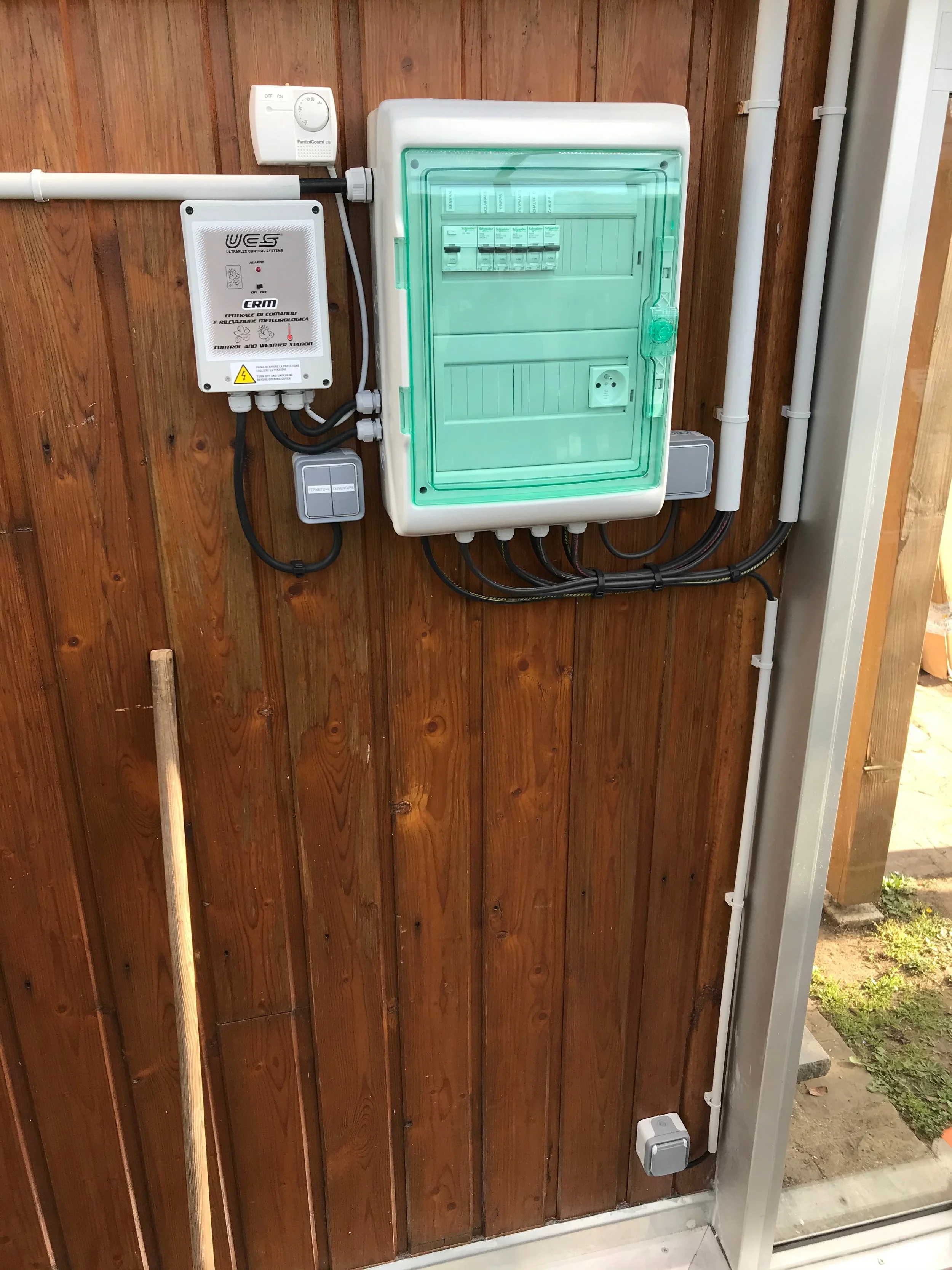 Installation électrique avec un tableau de distribution, un contrôleur, et des câbles fixés sur un mur en bois.