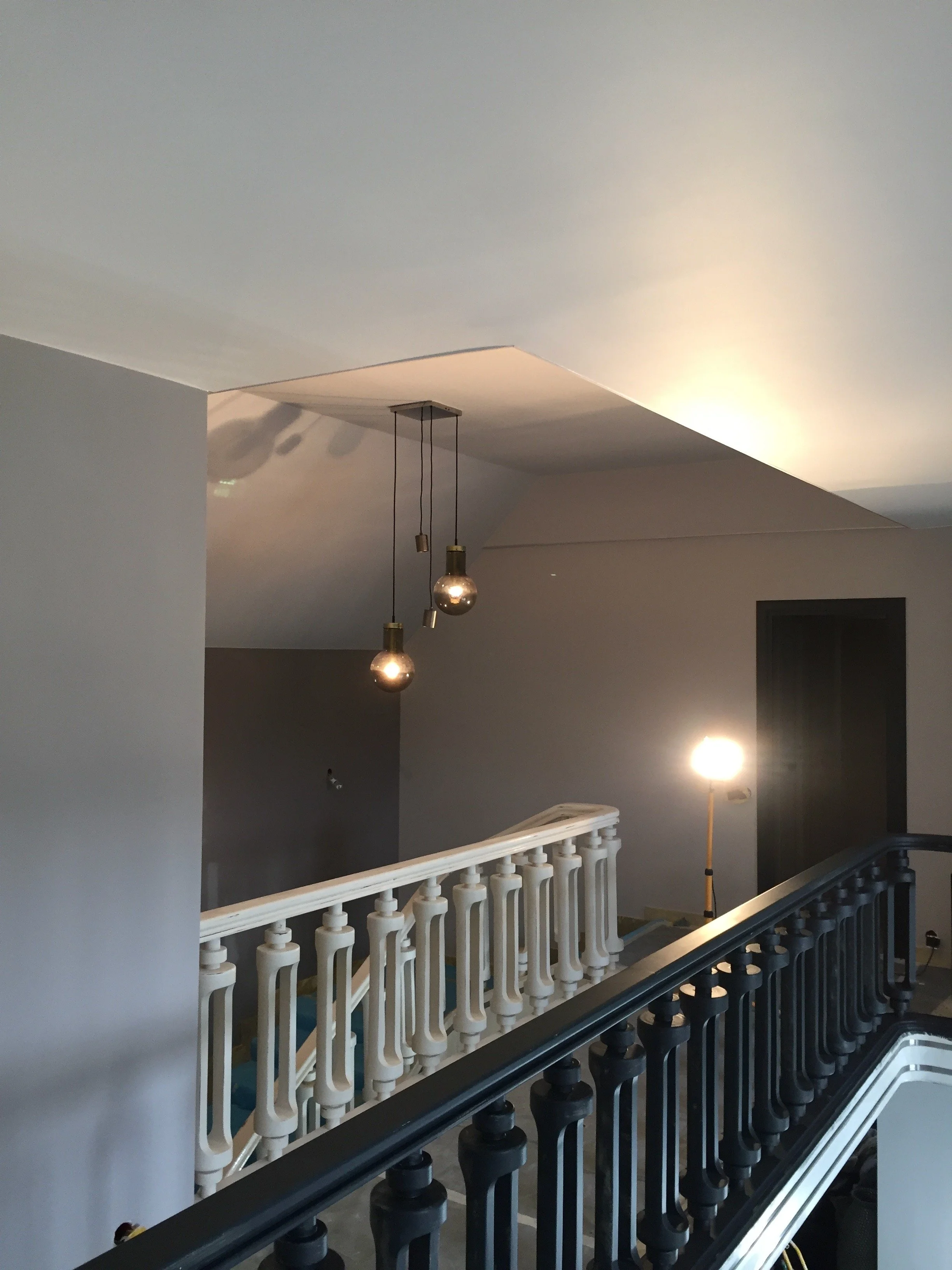 Intérieur d’un bâtiment en construction avec des escaliers, des lampes suspendues et un éclairage de travail