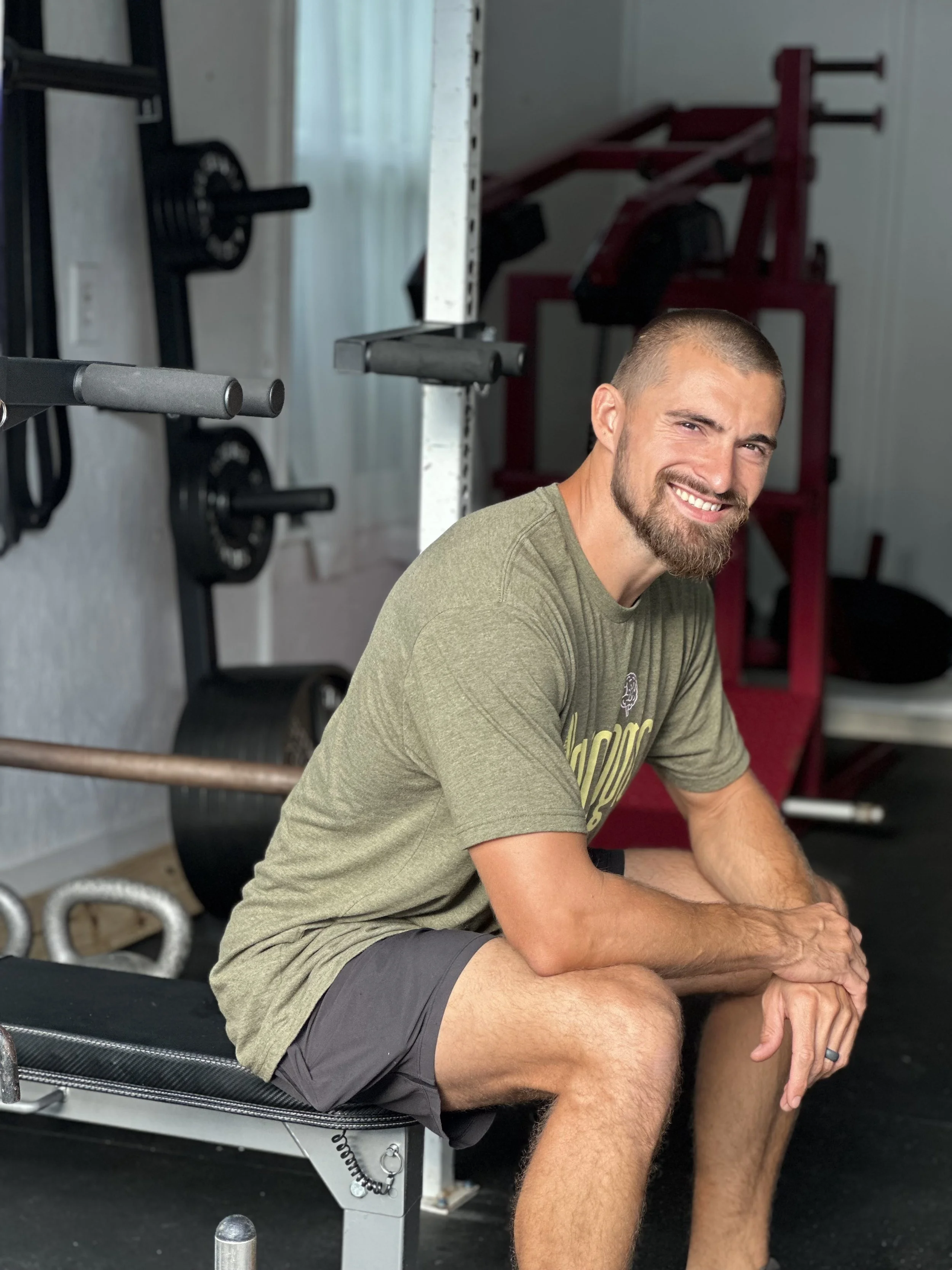 Owner of Neurologic Fitness Training Systems sitting on weight bench in weight room about to perform upper body exercise.