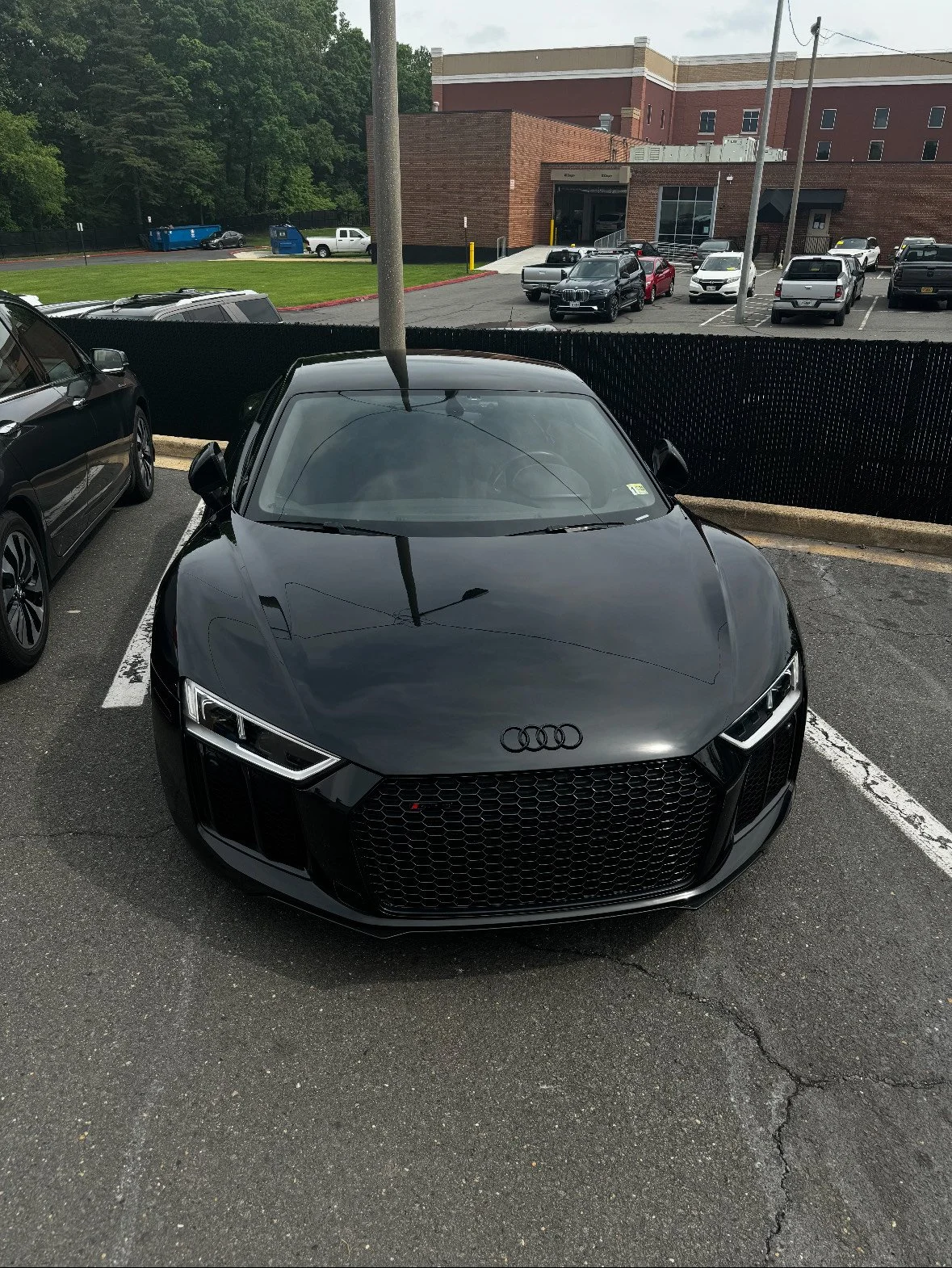 A black Audi sports car parked in a parking lot, with a building and other parked cars in the background.