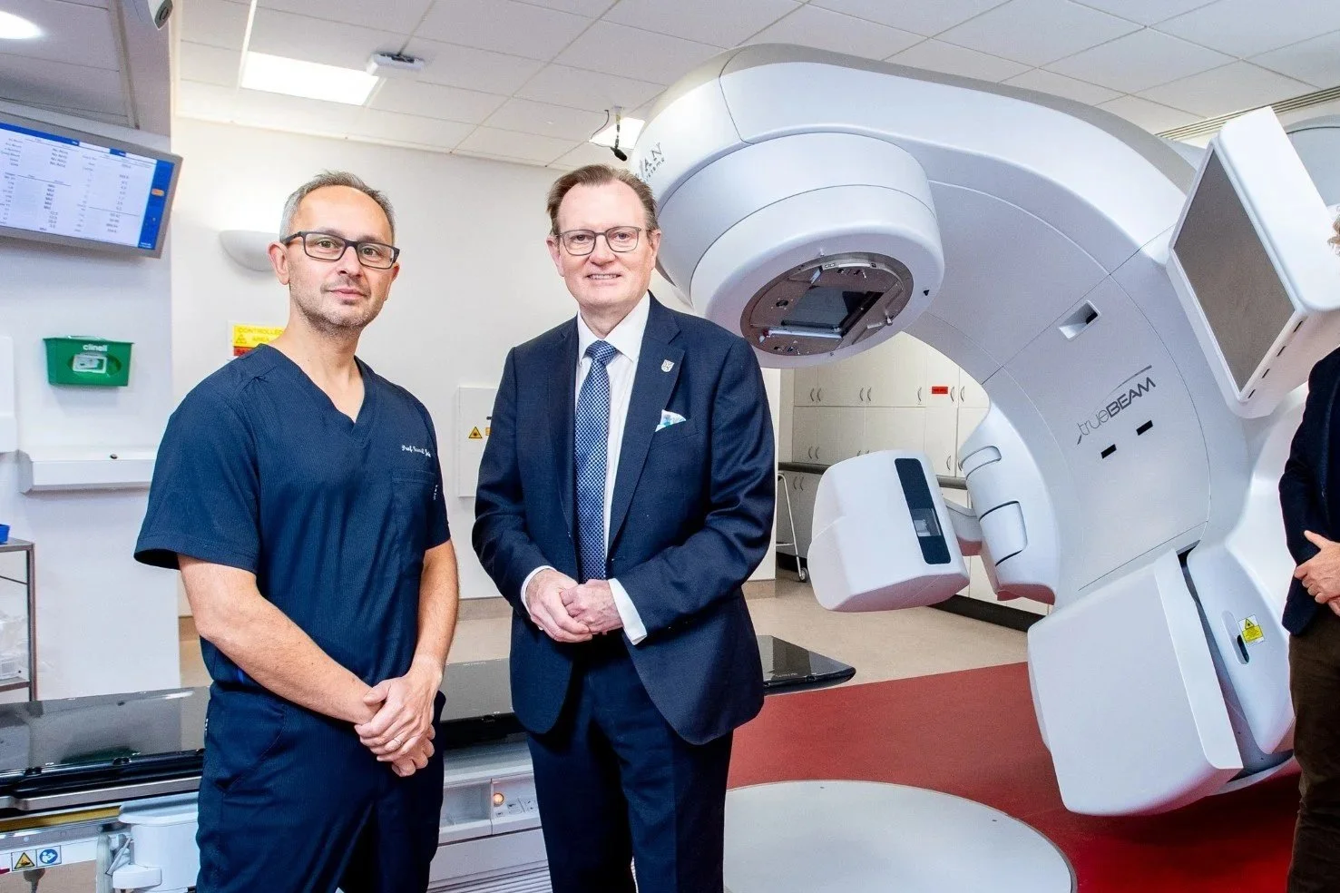Two men standing in a medical room with a large MRI machine in the background.