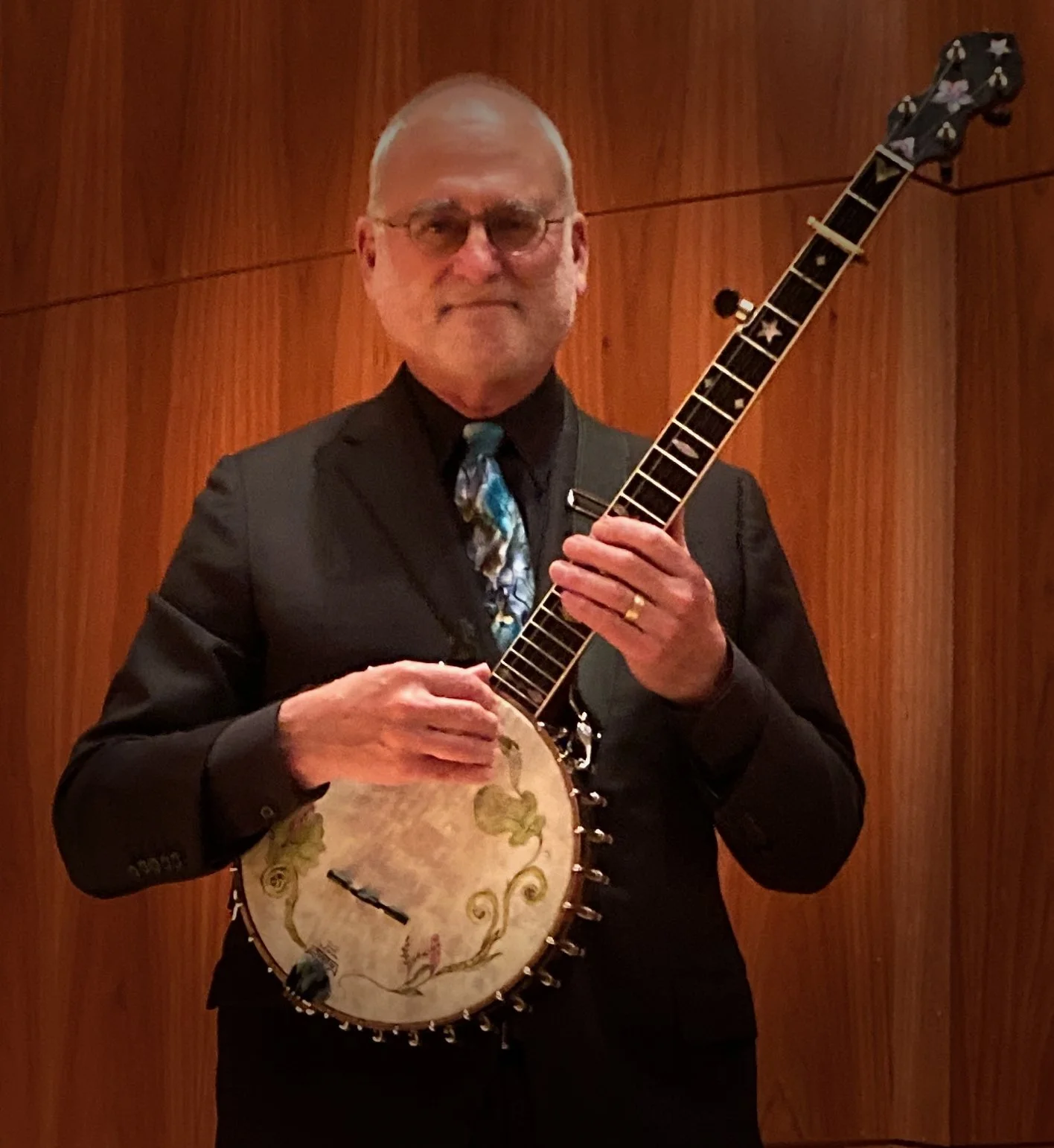 An older man with minimal gray hair softly smiling holding a banjo.