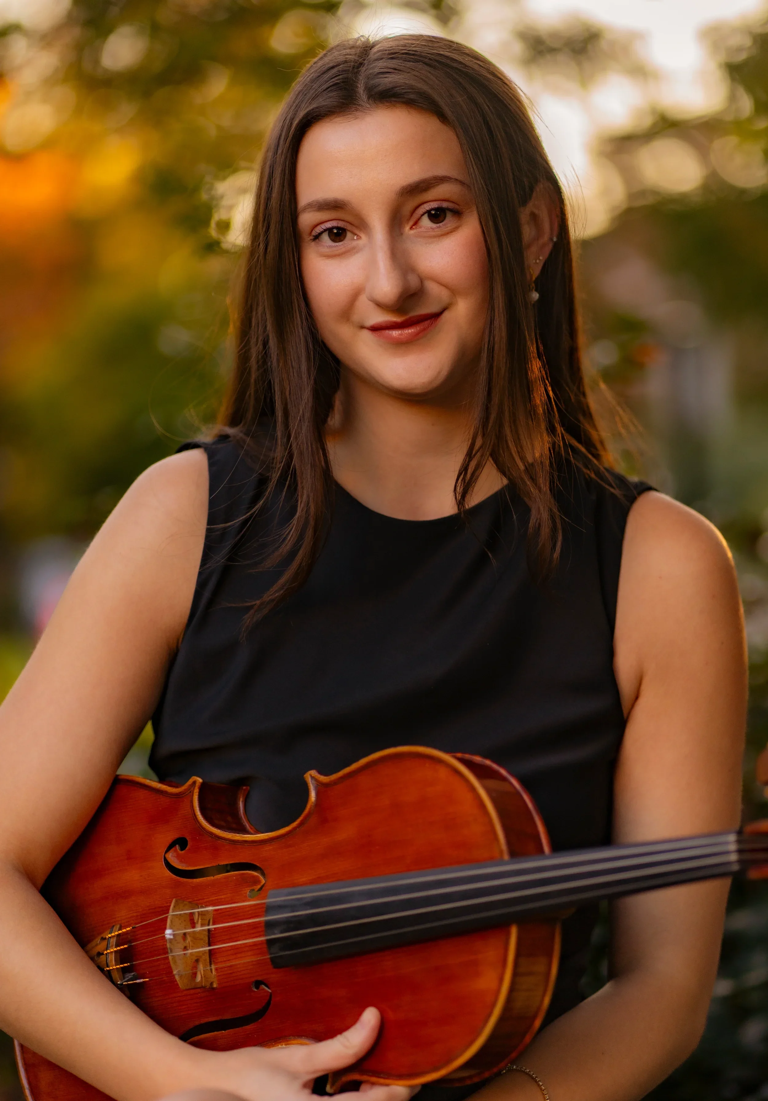 A Young Woman with brown hair smiling while holding a Viola.
