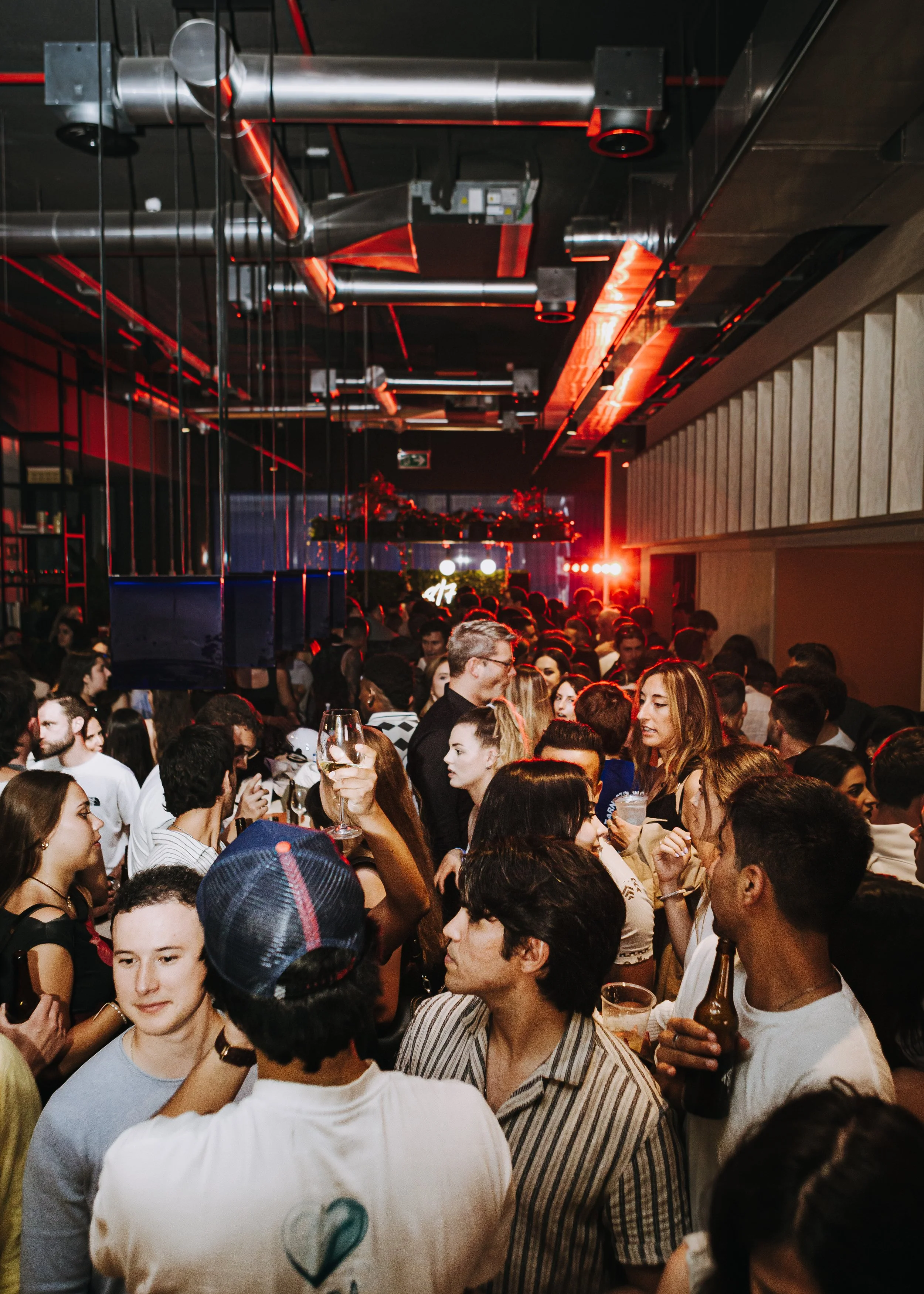 Una multitud de personas en un evento social en un espacio cerrado con decoraciones y luces rojo neón.