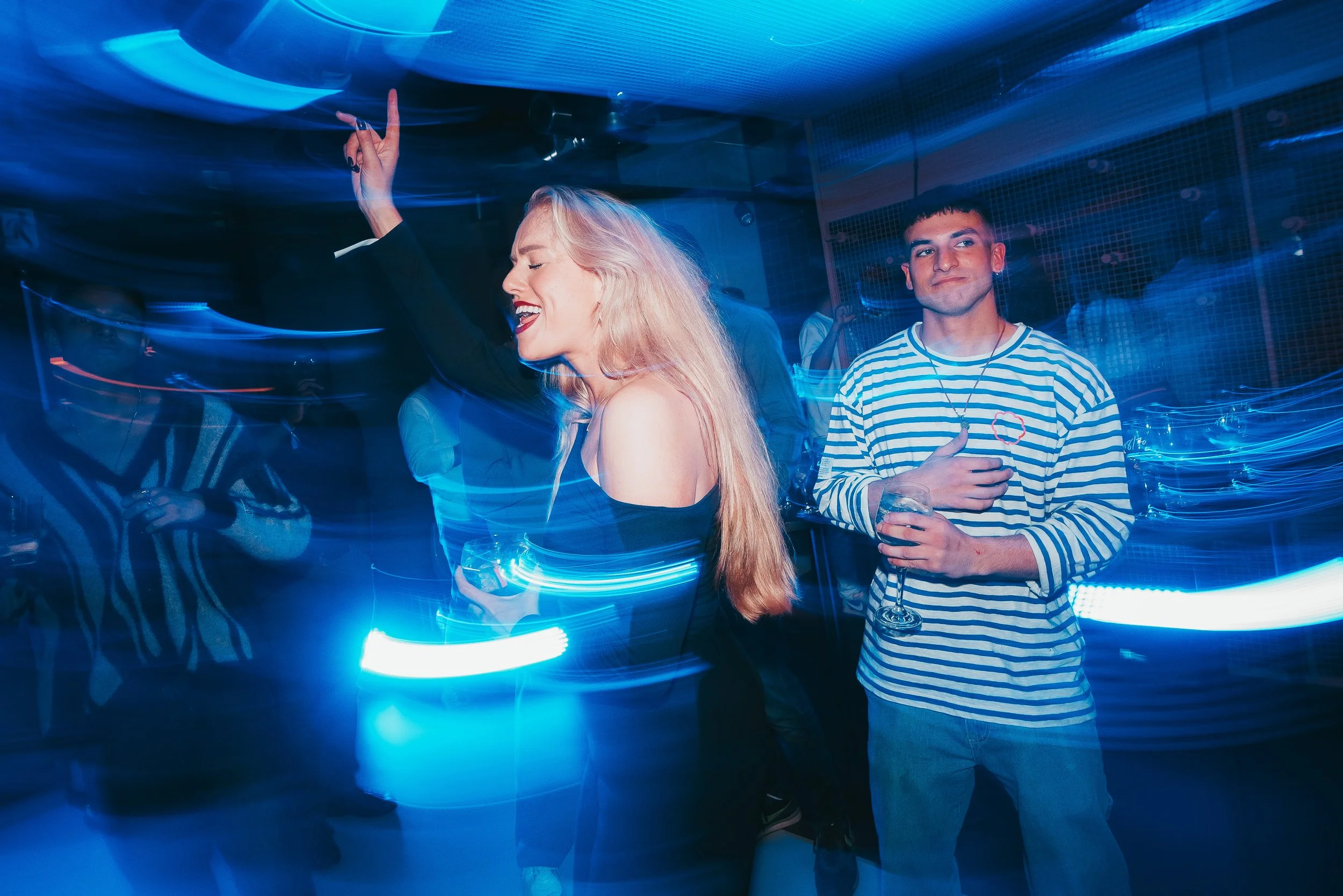 Personas bailando y disfrutando en una fiesta con luces de colores y ambiente vibrante.