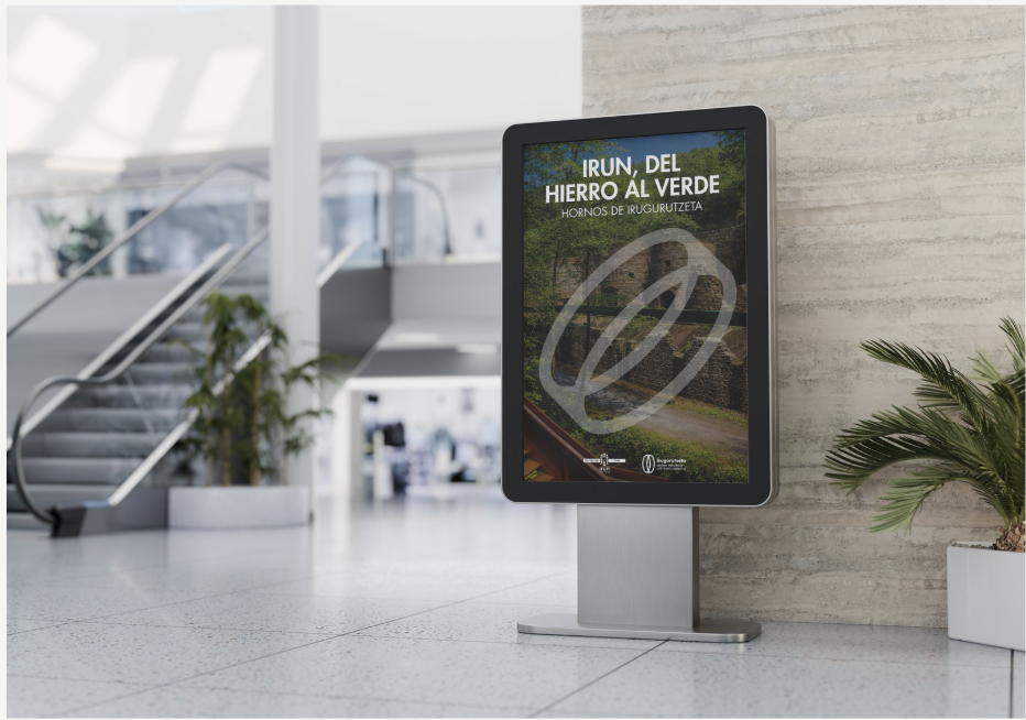 Pantalla digital en un espacio moderno con plantas, que muestra una publicación sobre irun, del hierro al verde, hornos de inugurutzeta.