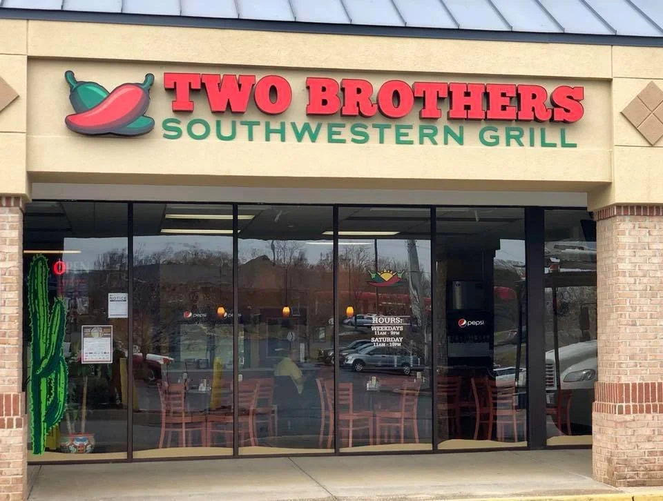 Front of Two Brothers Southwestern Grill restaurant with a cactus decoration on the window and a sign showing the hours of operation.