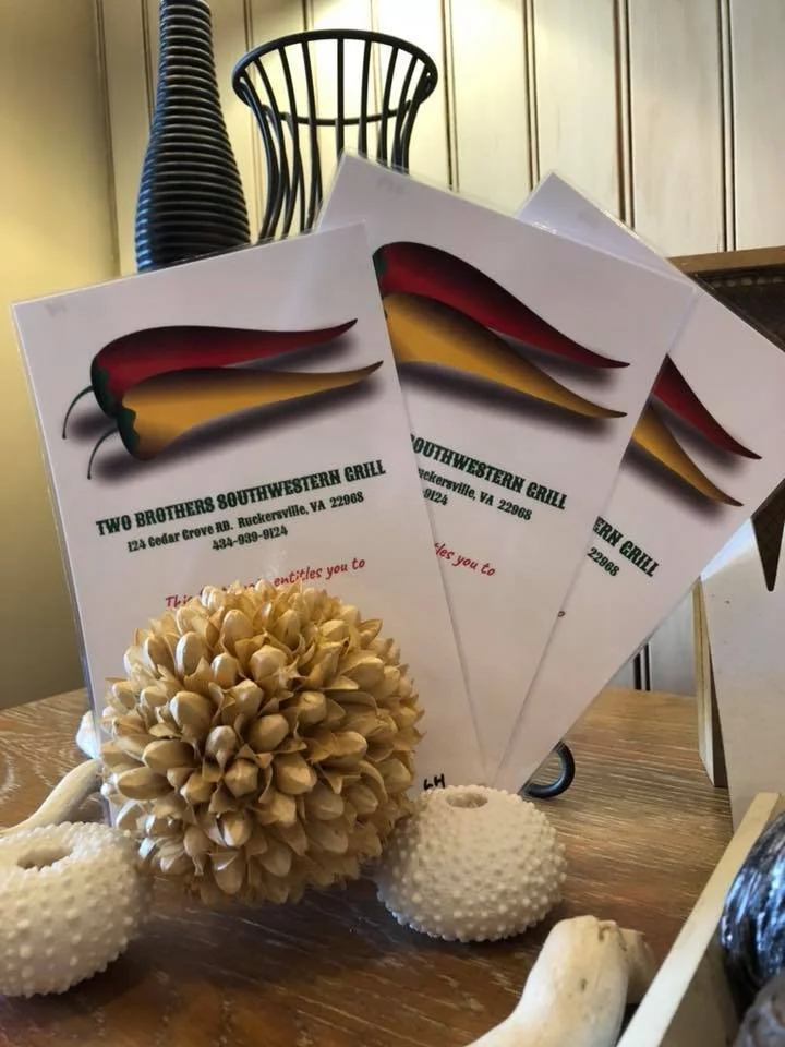 Three takeout menus for Two Brothers Southwestern Grill, featuring red and yellow chili peppers on the cover, arranged on a wooden surface.