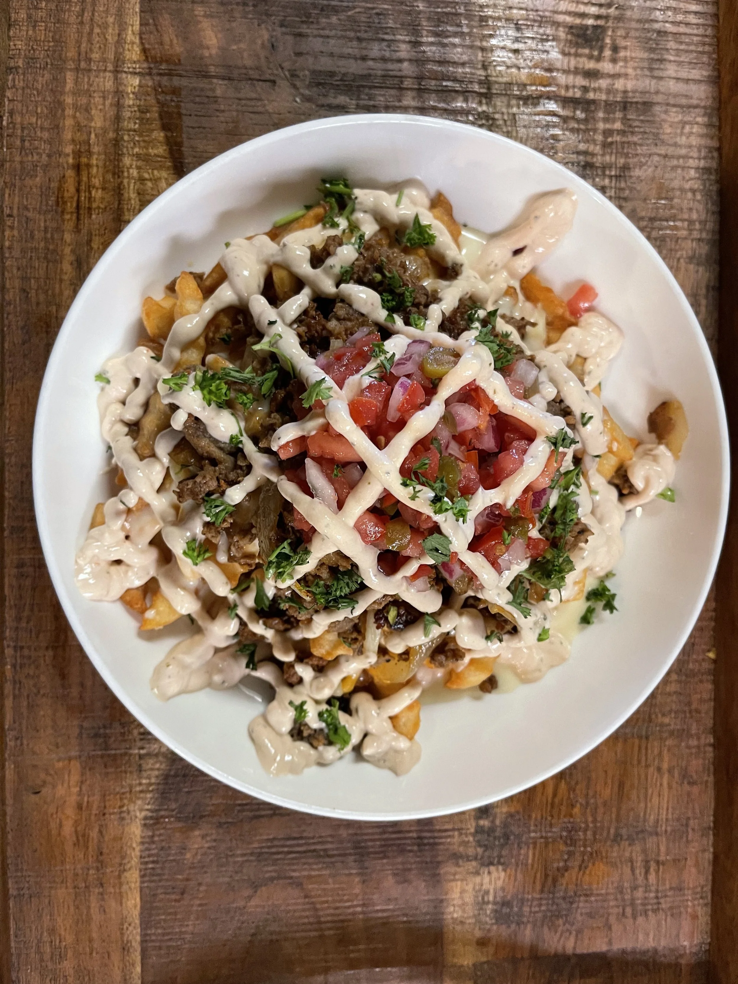 Plate of loaded nachos with cheese, ground beef, diced tomatoes, onions, and chopped cilantro.