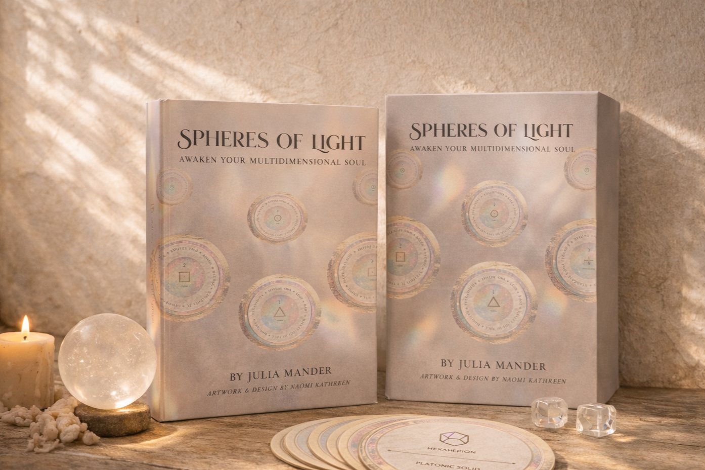 Two copies of a book titled "Spheres of Light" by Julia Mander, placed on a wooden surface with candles, crystals, and holographic cards in a warm, softly lit setting.