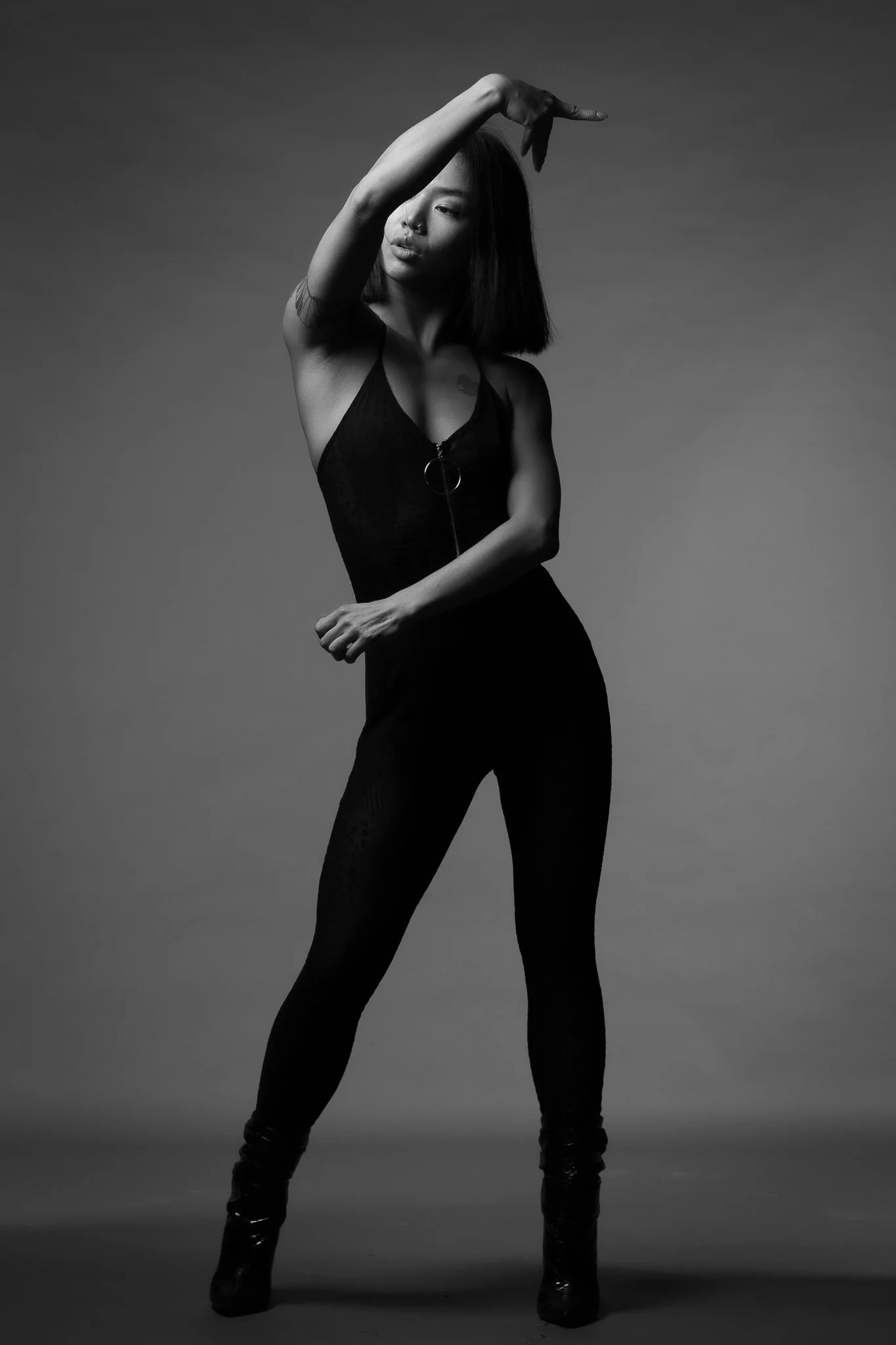 A woman in black clothing posing against a plain backdrop.