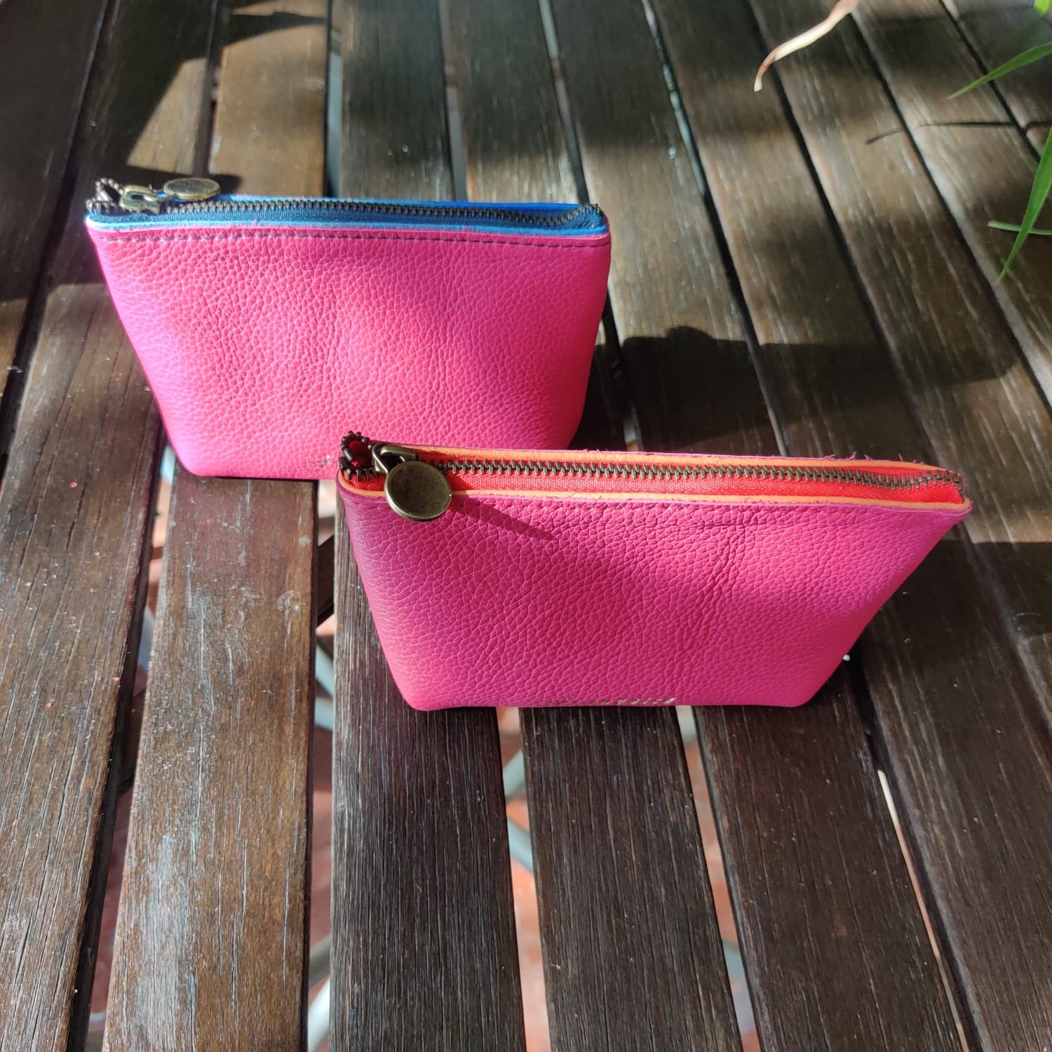 Two pink textured zippered mini wallets with metal zipper pulls on a wooden surface.