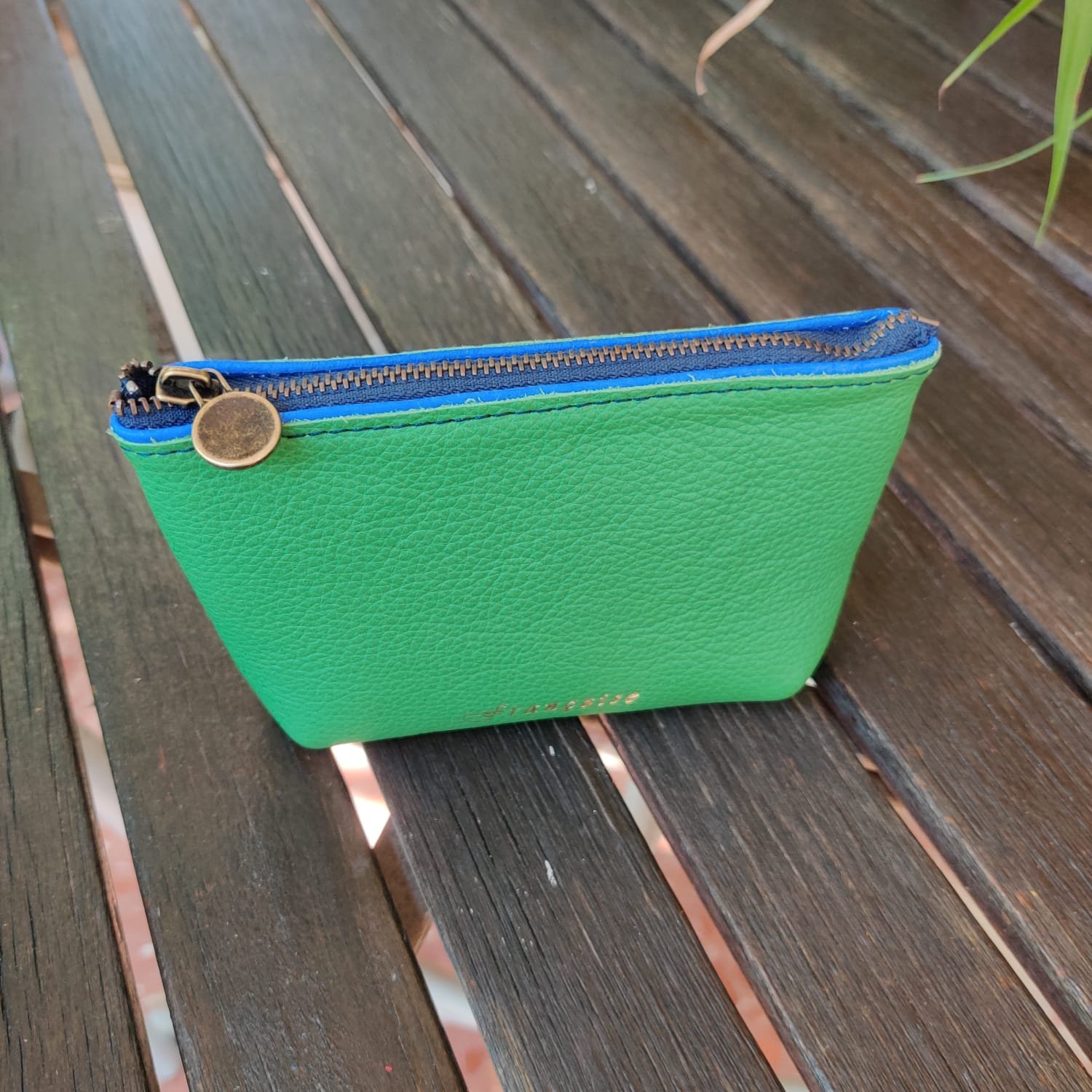 Green and blue zippered mini wallet with a zipper on a wooden surface.