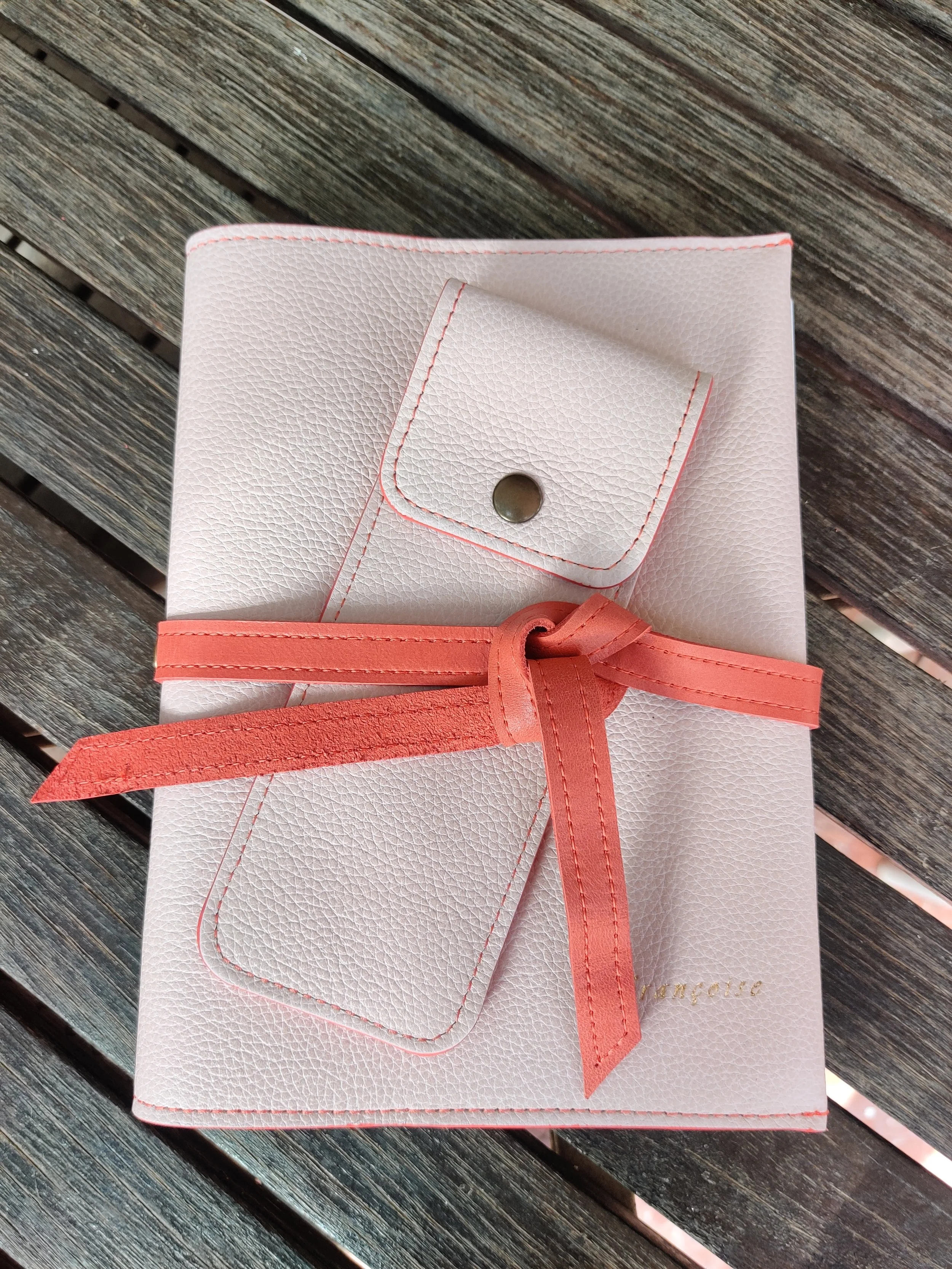 A pink notebook closed with a ribbon, placed on a wooden surface. 
