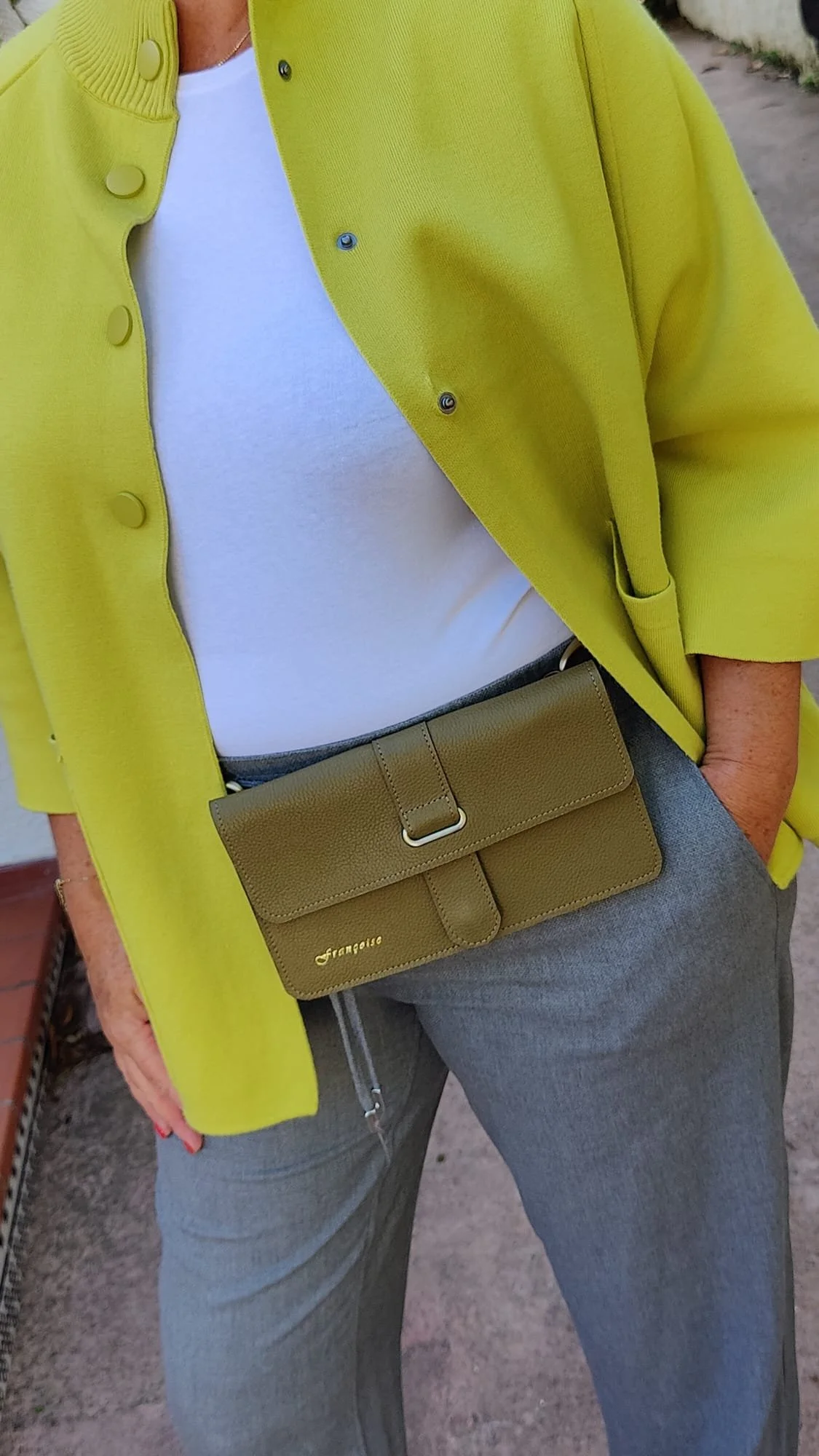 Person wearing a colourful jacket, carrying a dark green Françoise City leather handbag around the waist.