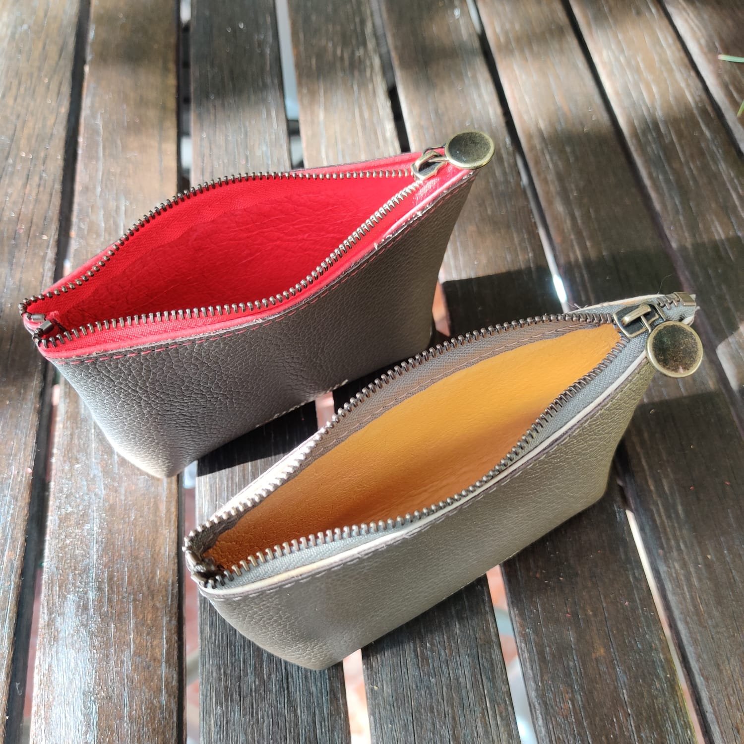 Two mini wallets, one with a red interior and the other with a yellow interior, are placed on a wooden surface.
