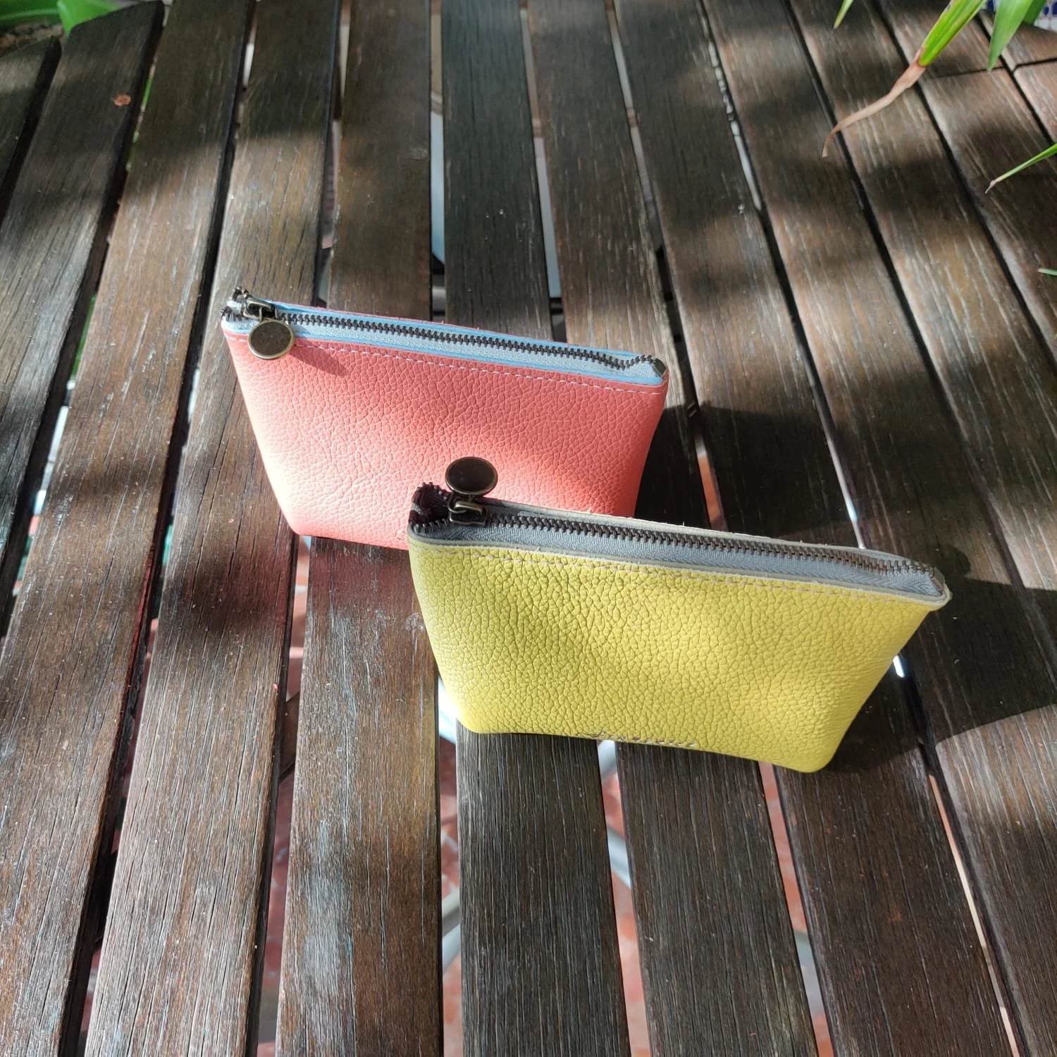 A pink and a yellow mini leather wallets on a wooden picnic table.