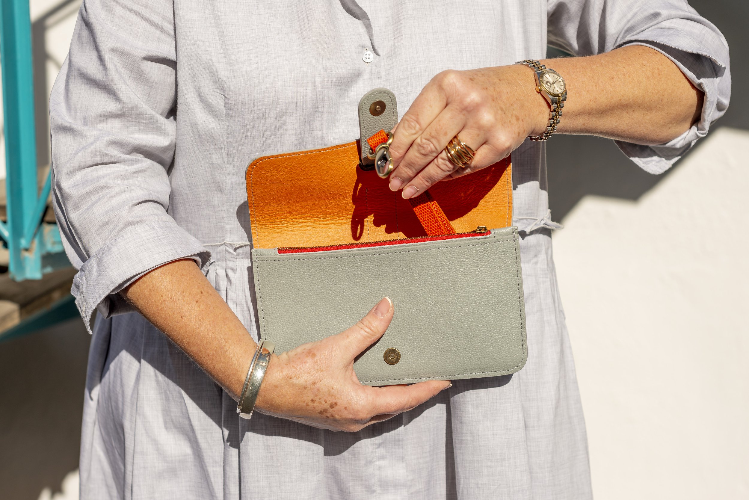 A person in a light gray shirt holding a gray Françoise City leather handbag with a snap button, revealing an orange inside.
