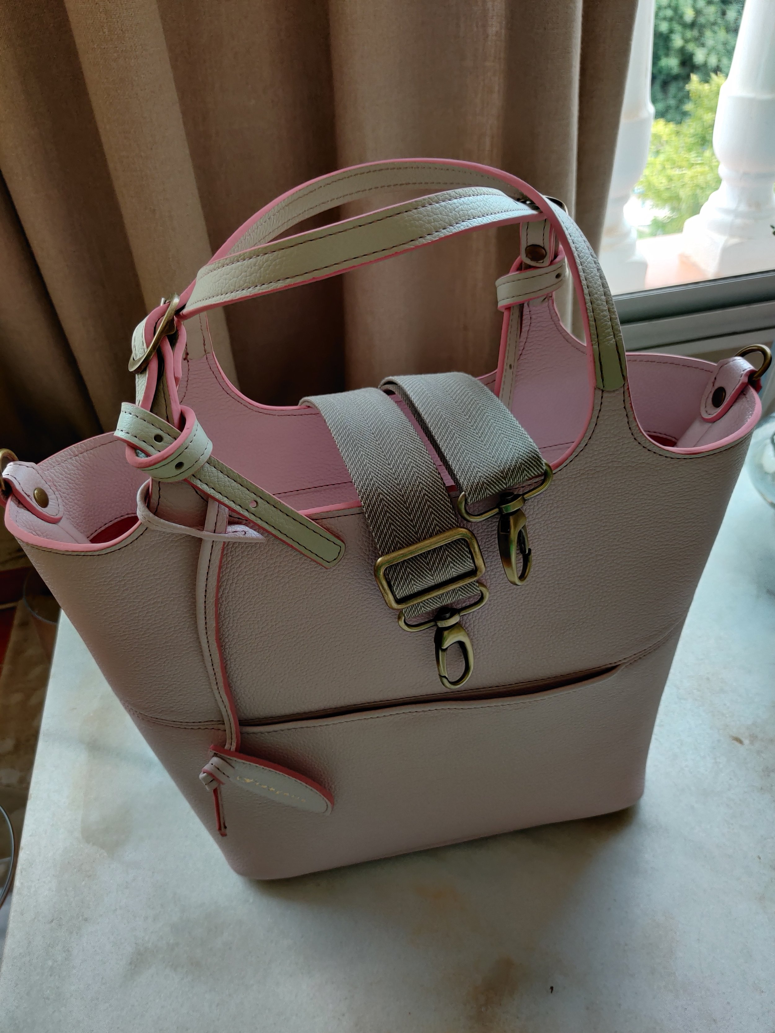 A Francoise Choco Late leather handbag with a pink inside sitting on a table near a window.