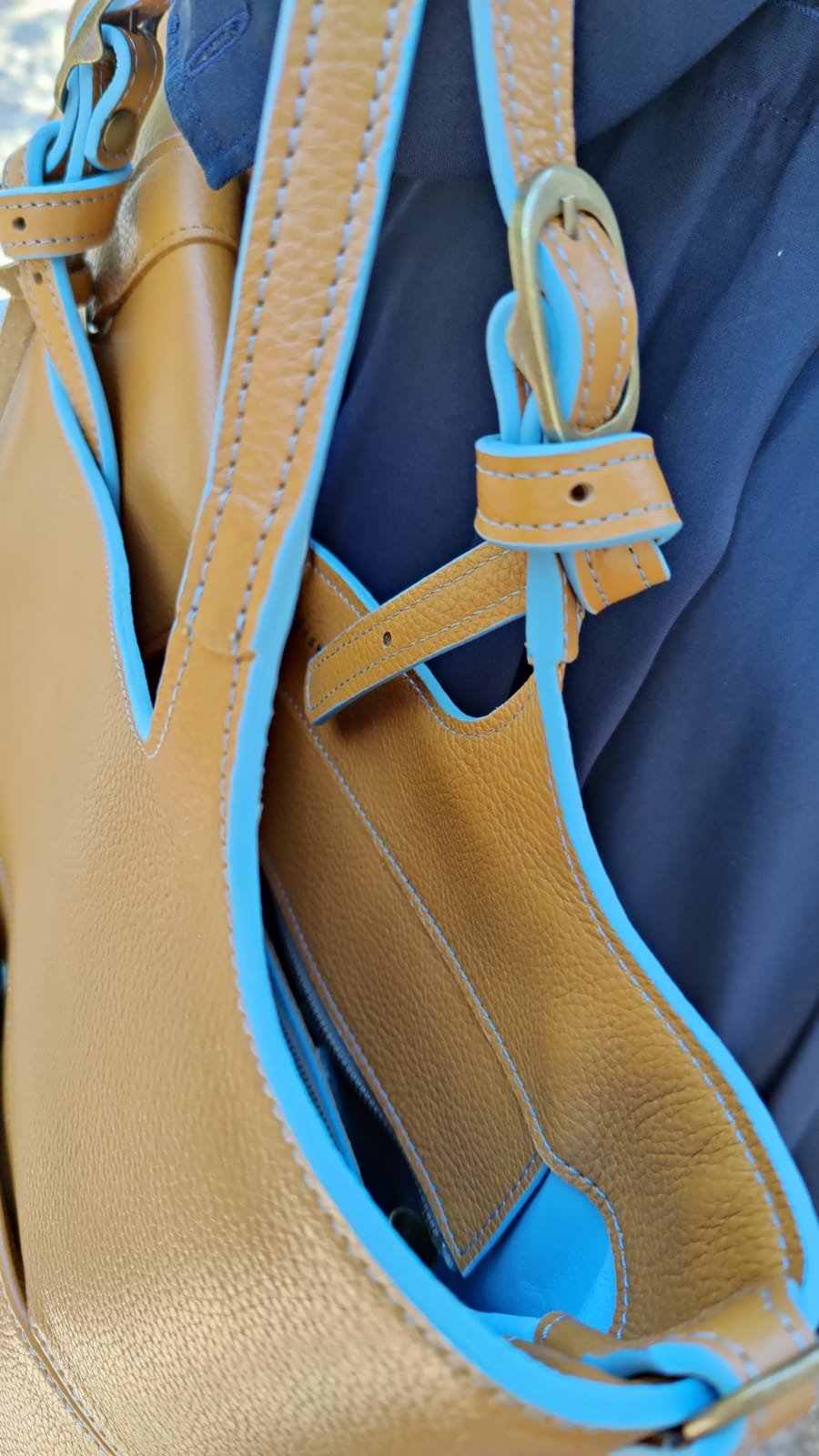 Close-up of a tan Francoise Choco Late leather handbag with blue accents, resting on dark blue fabric. 