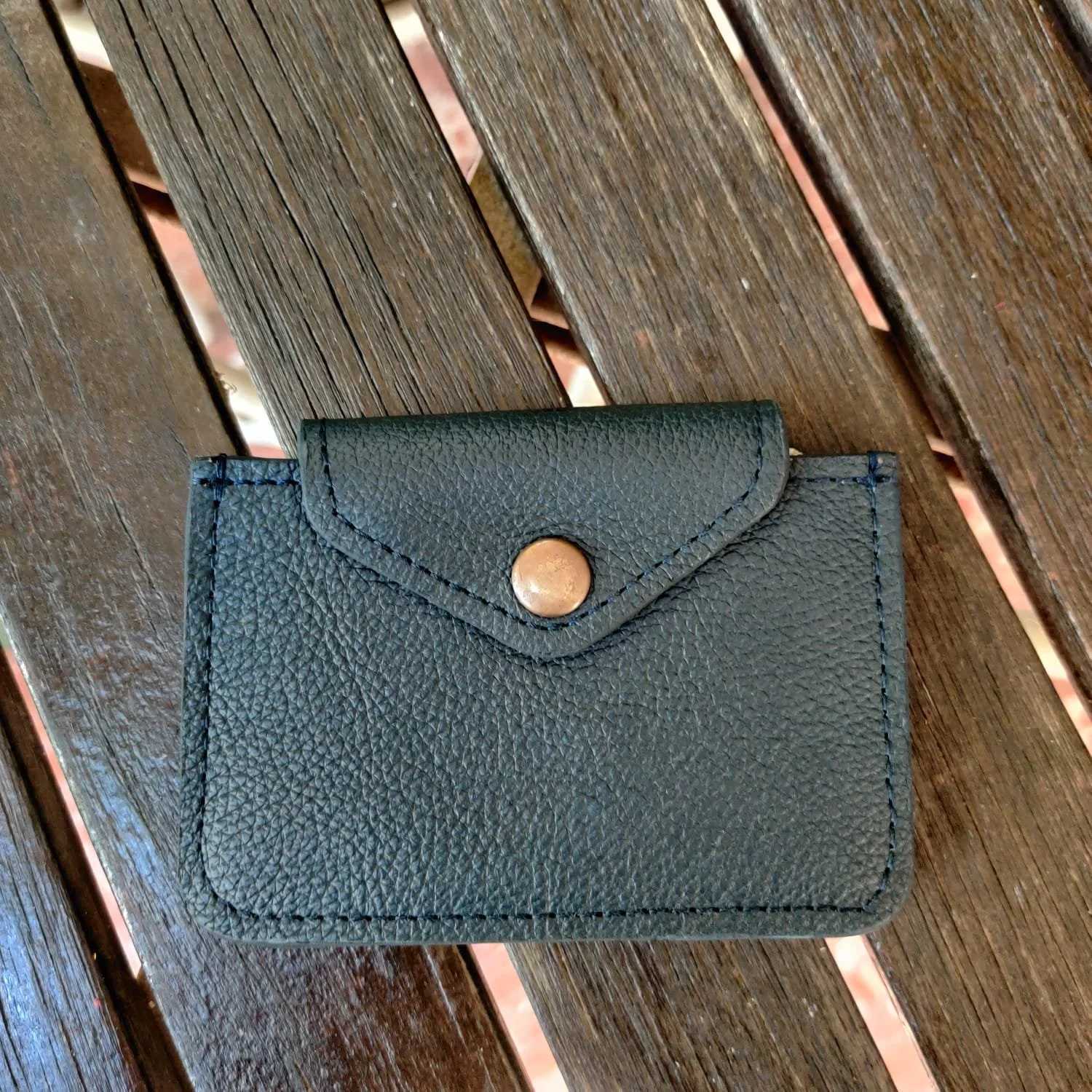 Black cardholder wallet with a snap closure resting on a wooden surface.