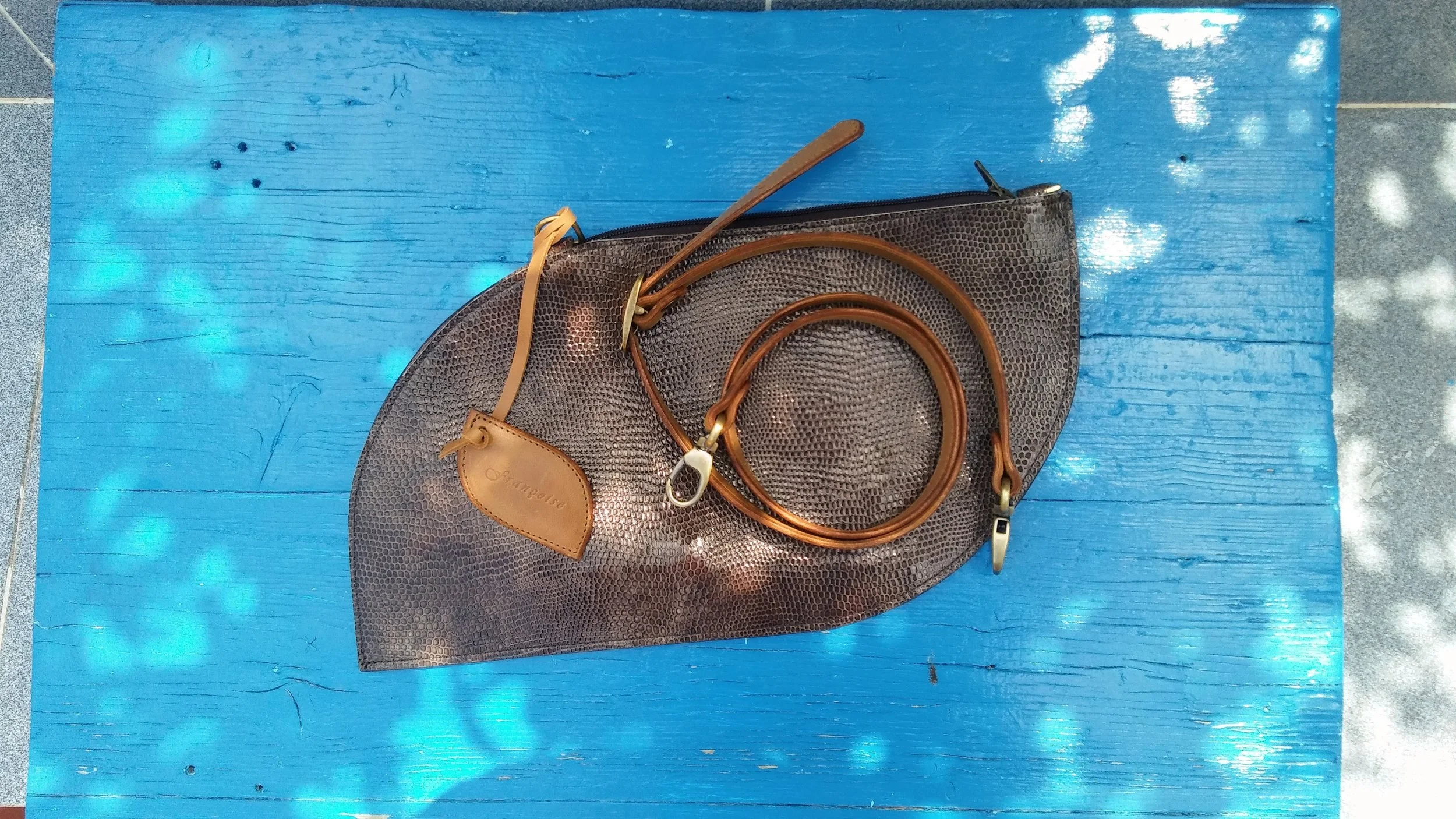 Françoise Crossbody leather handbag  Brown crocodile-patterned Françoise Cross Body leather handbag with brown leather belt, placed on a bright blue painted wooden surface. 