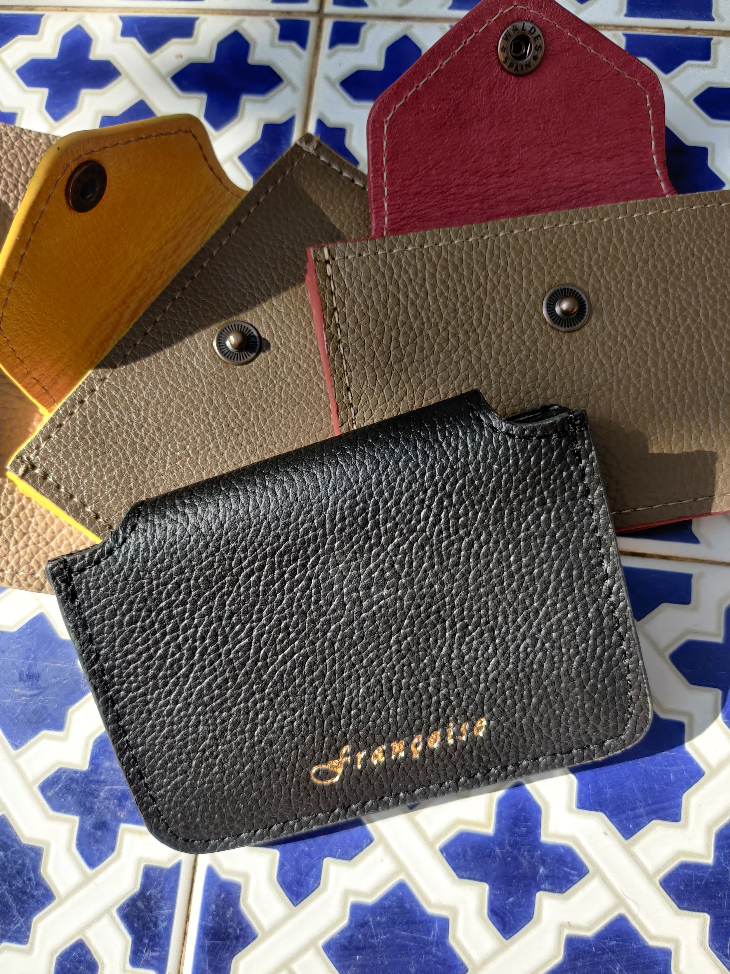 Four colorful leather cardholders with snap closures on a blue and white decorative tile surface.