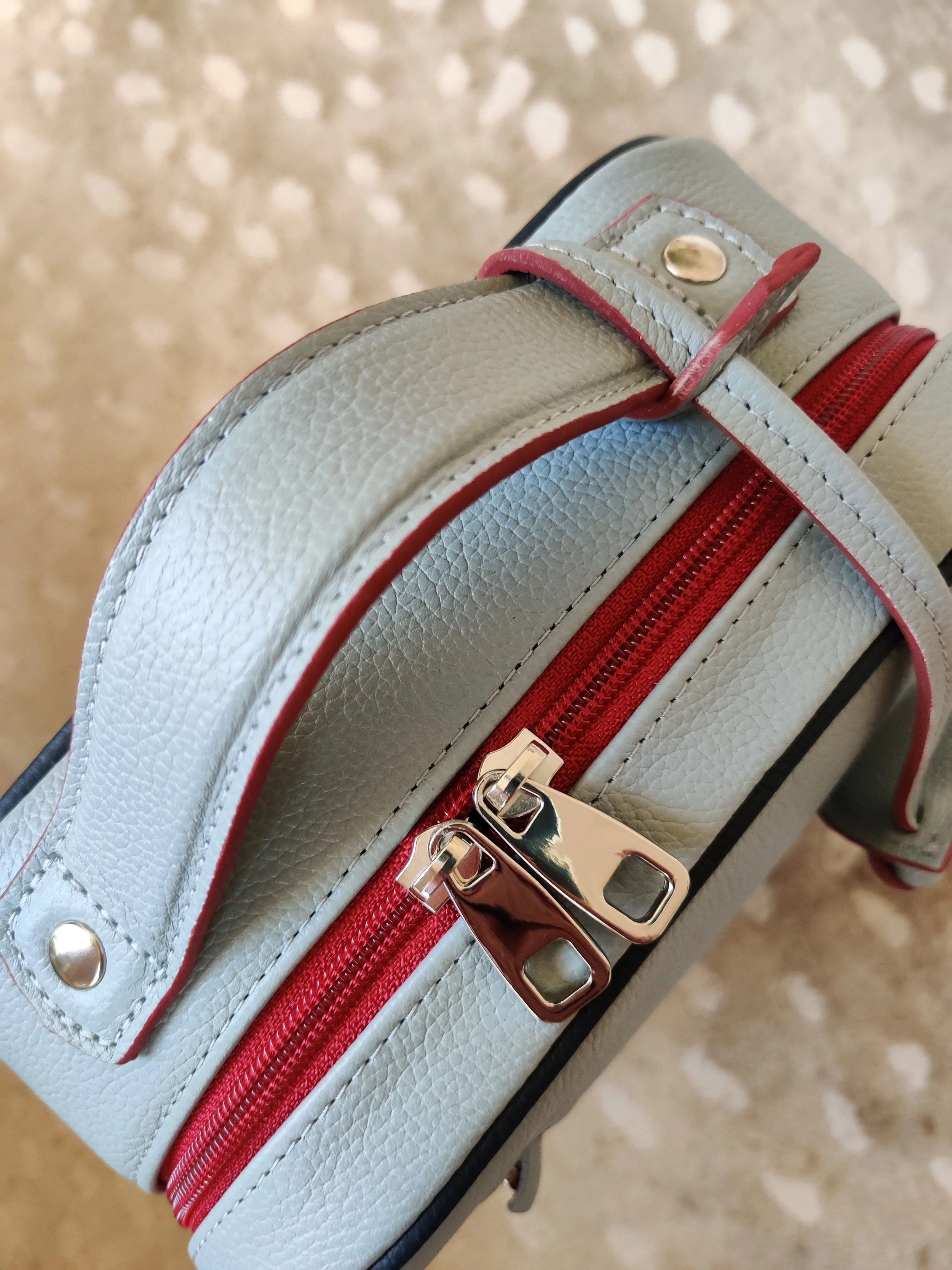 Close up of a Françoise Backpack with red zipper, on a beige surface.