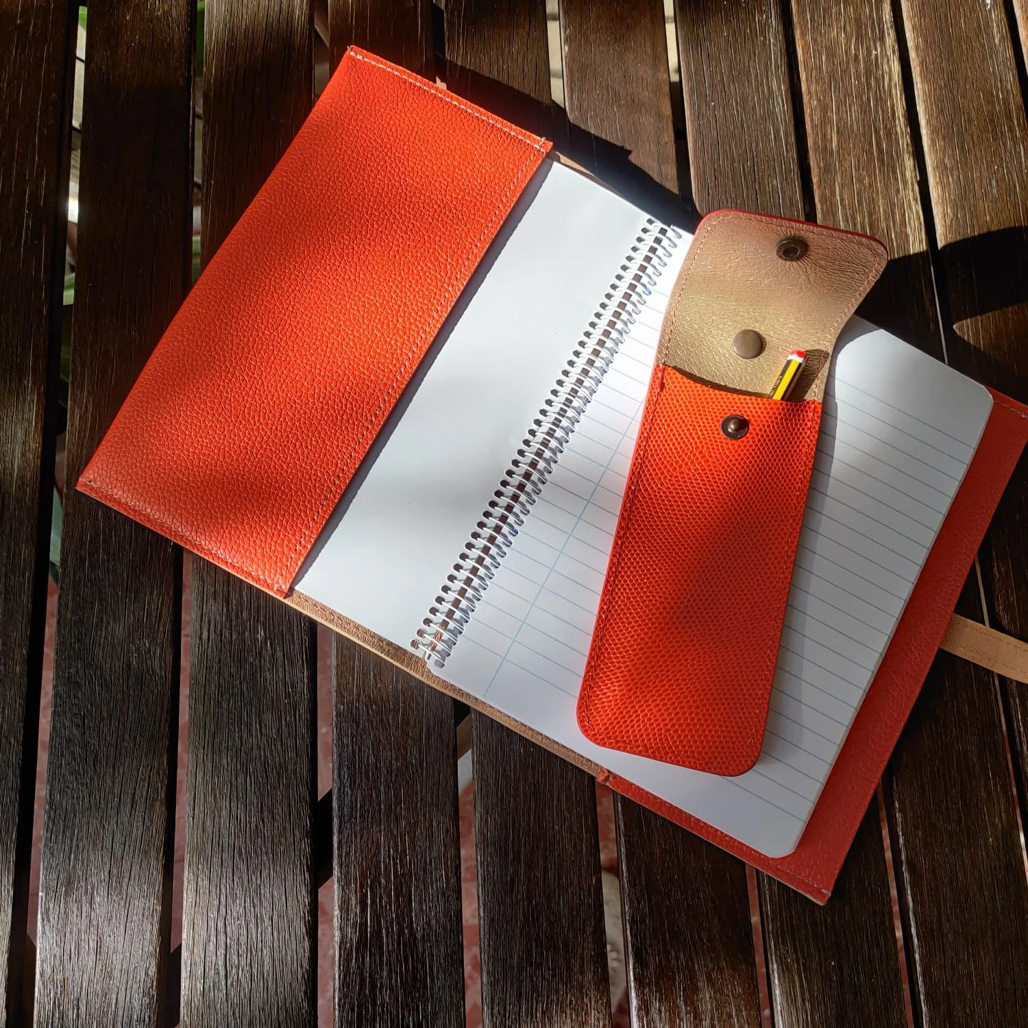 Open orange leather notebook with lined pages and a pen holder on a wooden surface.