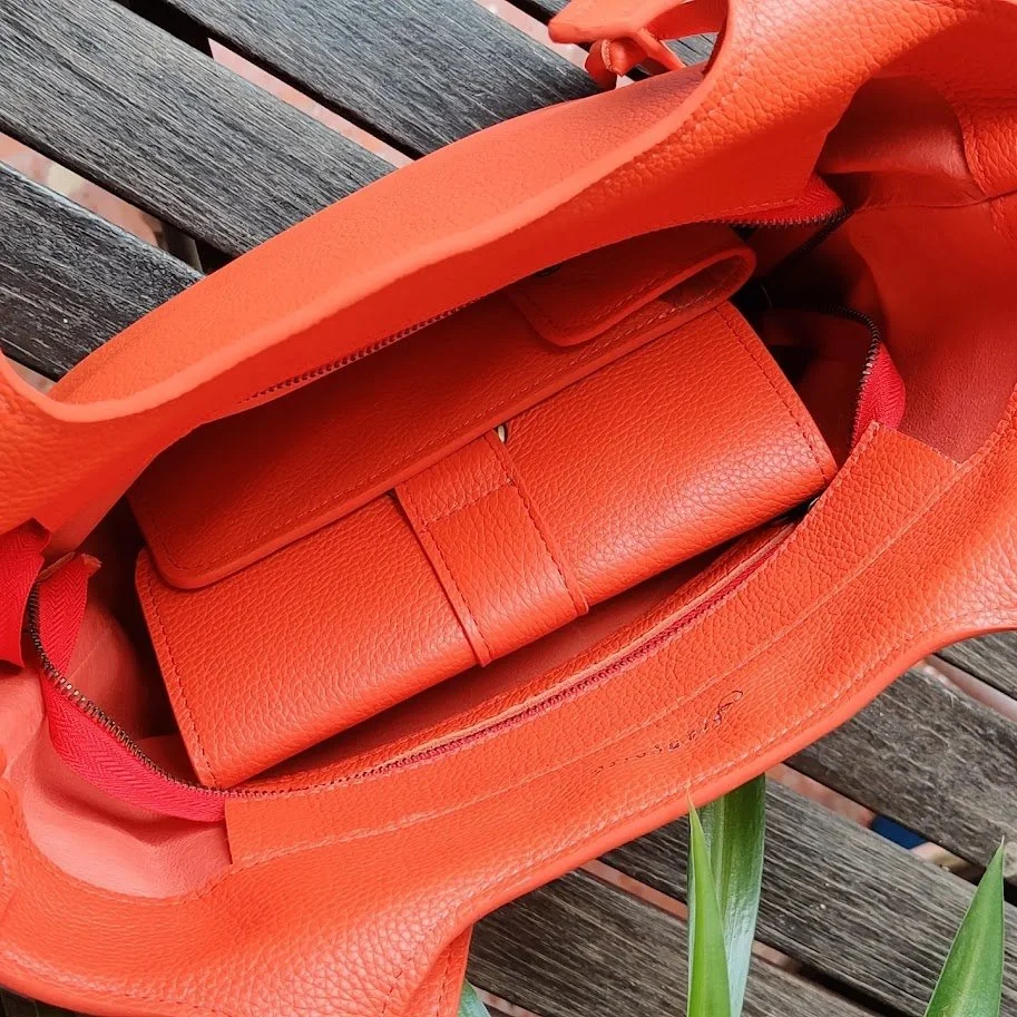 Image showing an Orange bag with a matching wallet inside, resting on a wooden bench outdoors.