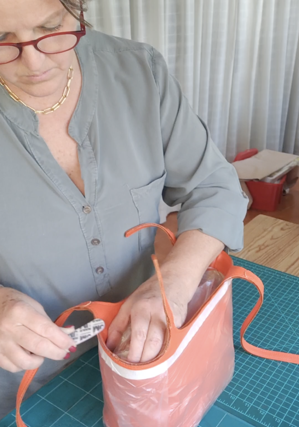 Francoise repairing a leather tote bag on a green cutting mat, with windows in the background.