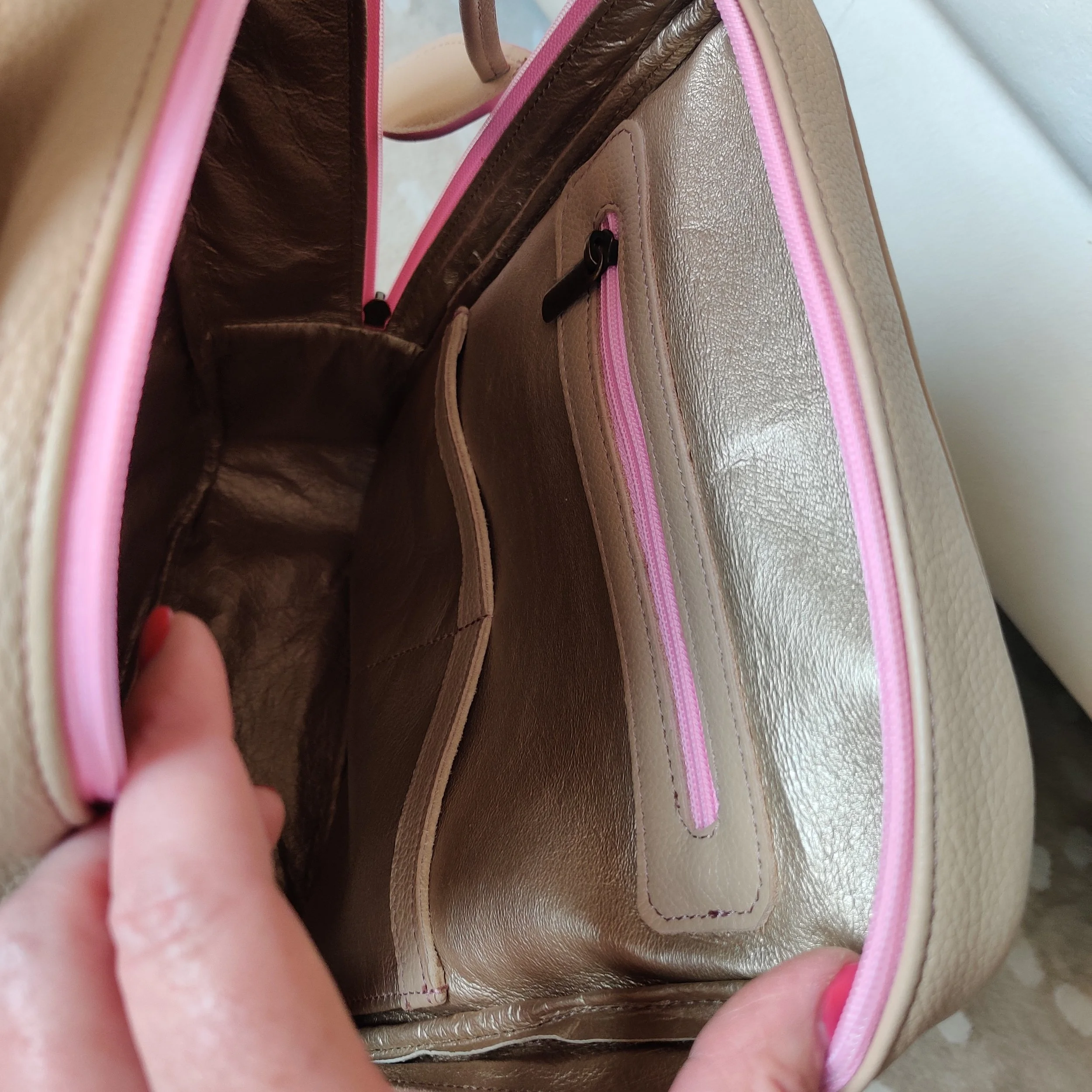 Close up of a Françoise Backpack with pink accents showing spacious interior, interior pockets, and zipper compartments.