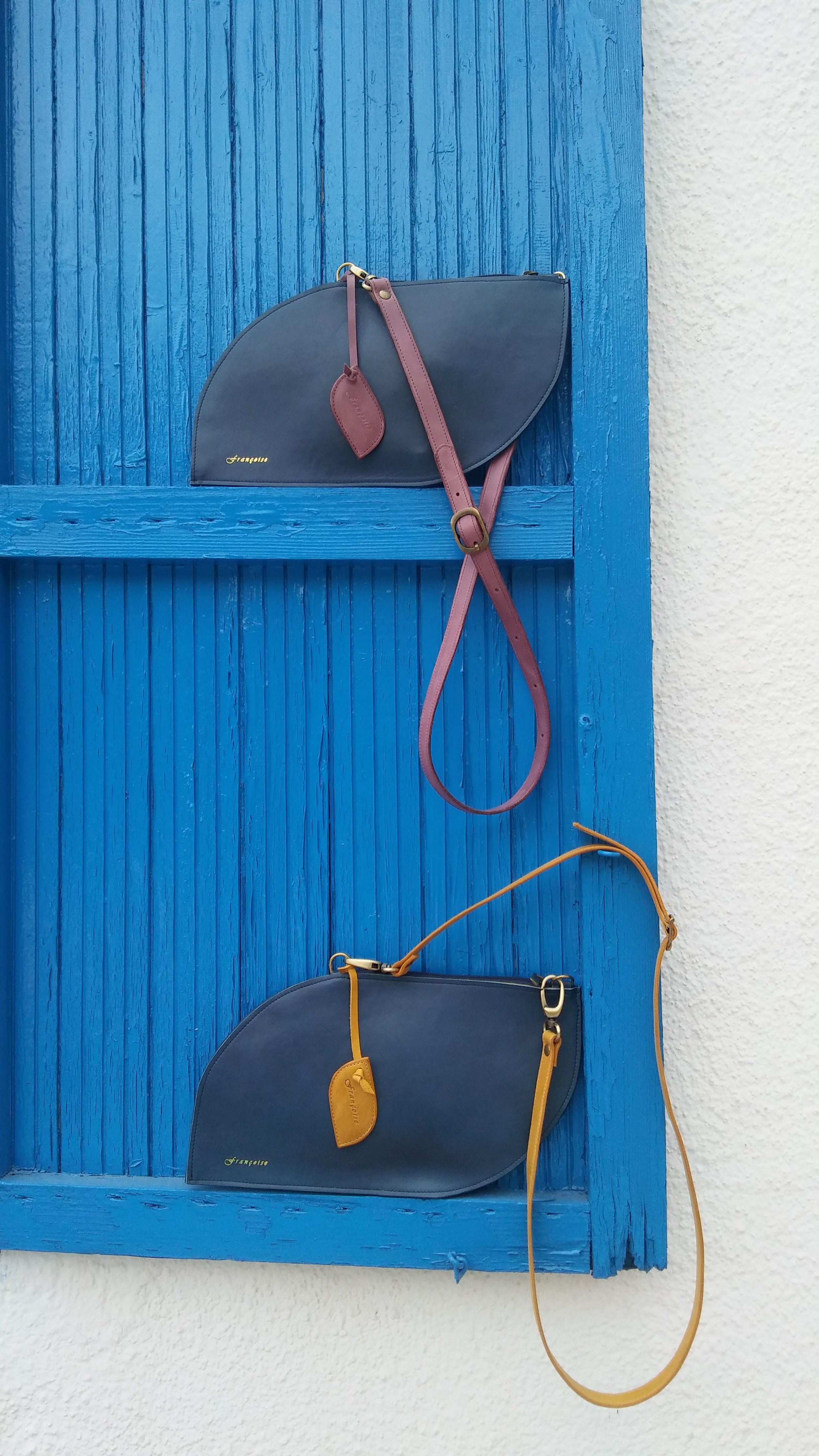 Navy blue Françoise Crossbody leather handbag with strap, resting on a bright blue wooden wall panel.