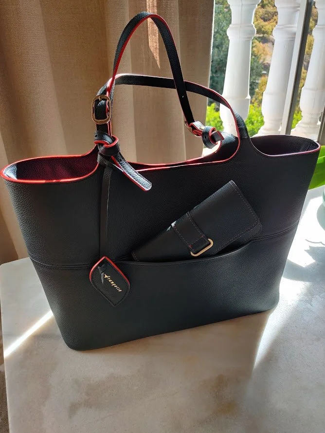 Black Françoise Fondant leather handbag with red accents, containing a wallet, placed on a table near a window with natural light.