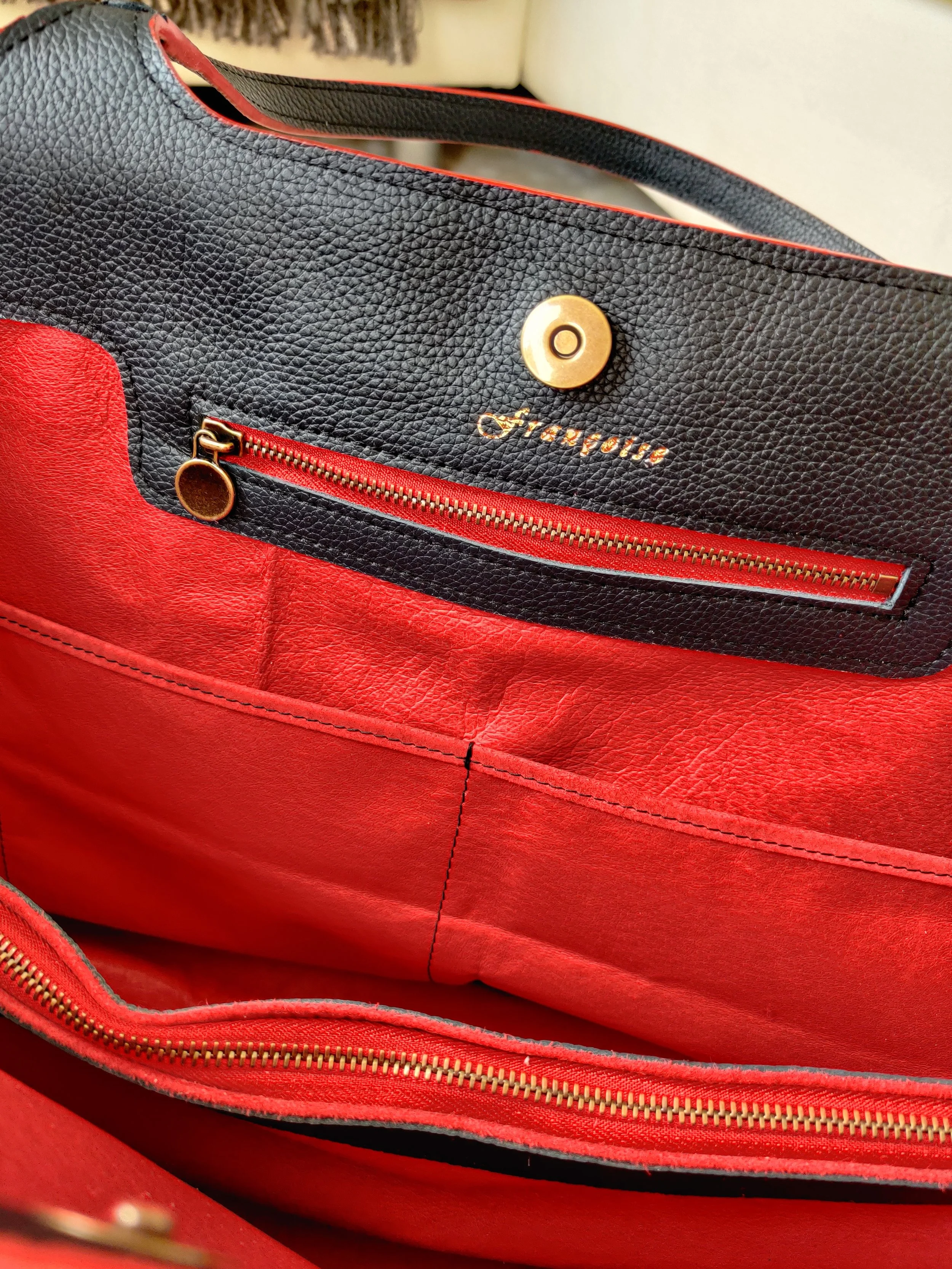 Close-up of a black Françoise Fondant leather handbag with red inside, showing pockets inside that can be closed with metal zippers. 