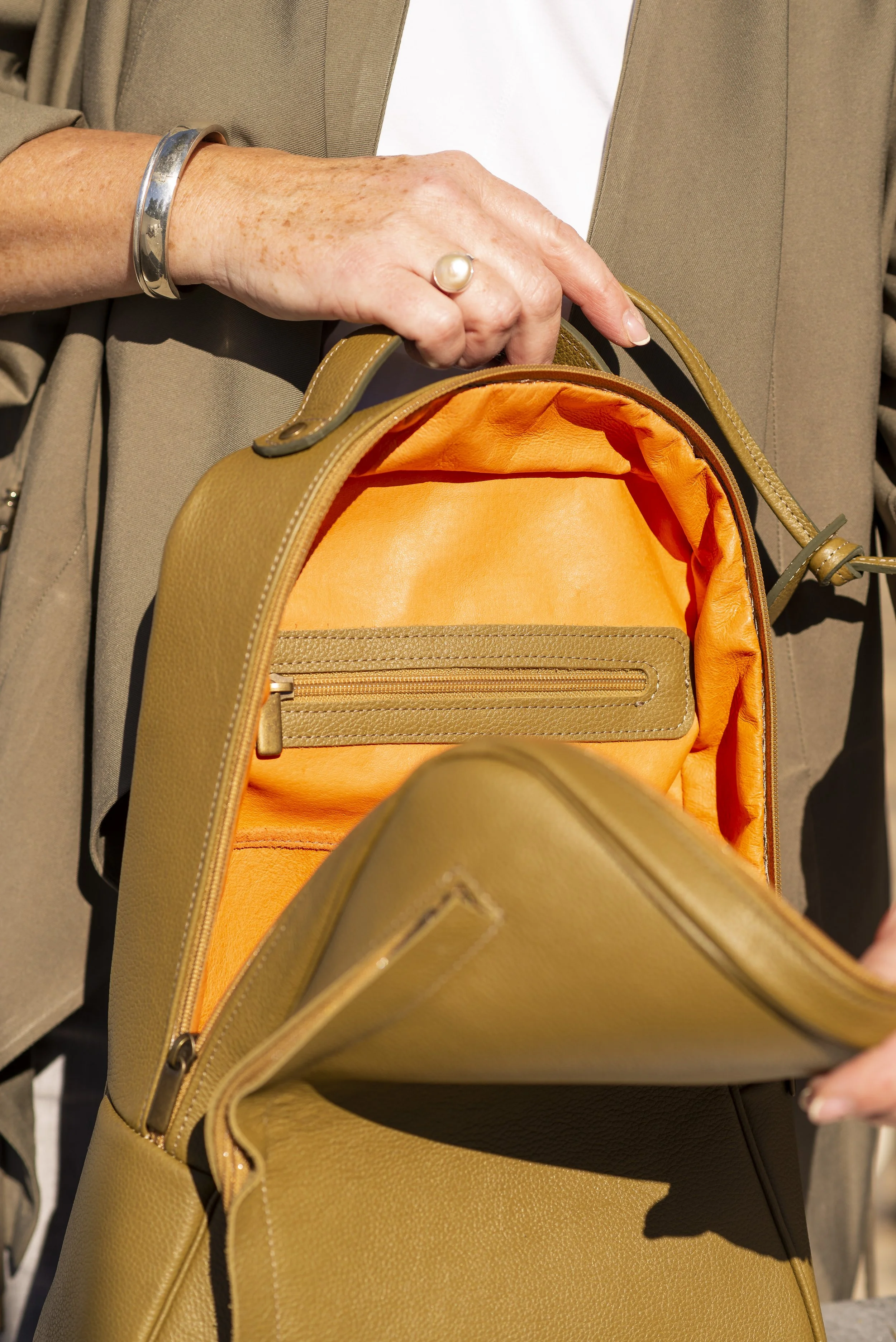 A person holding a light brown Françoise Backpack with an orange interior, showing the open bag's inside and a zippered pocket.