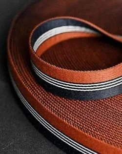 Close-up of a roll of striped canvas belt material in black, orange, and white colors.