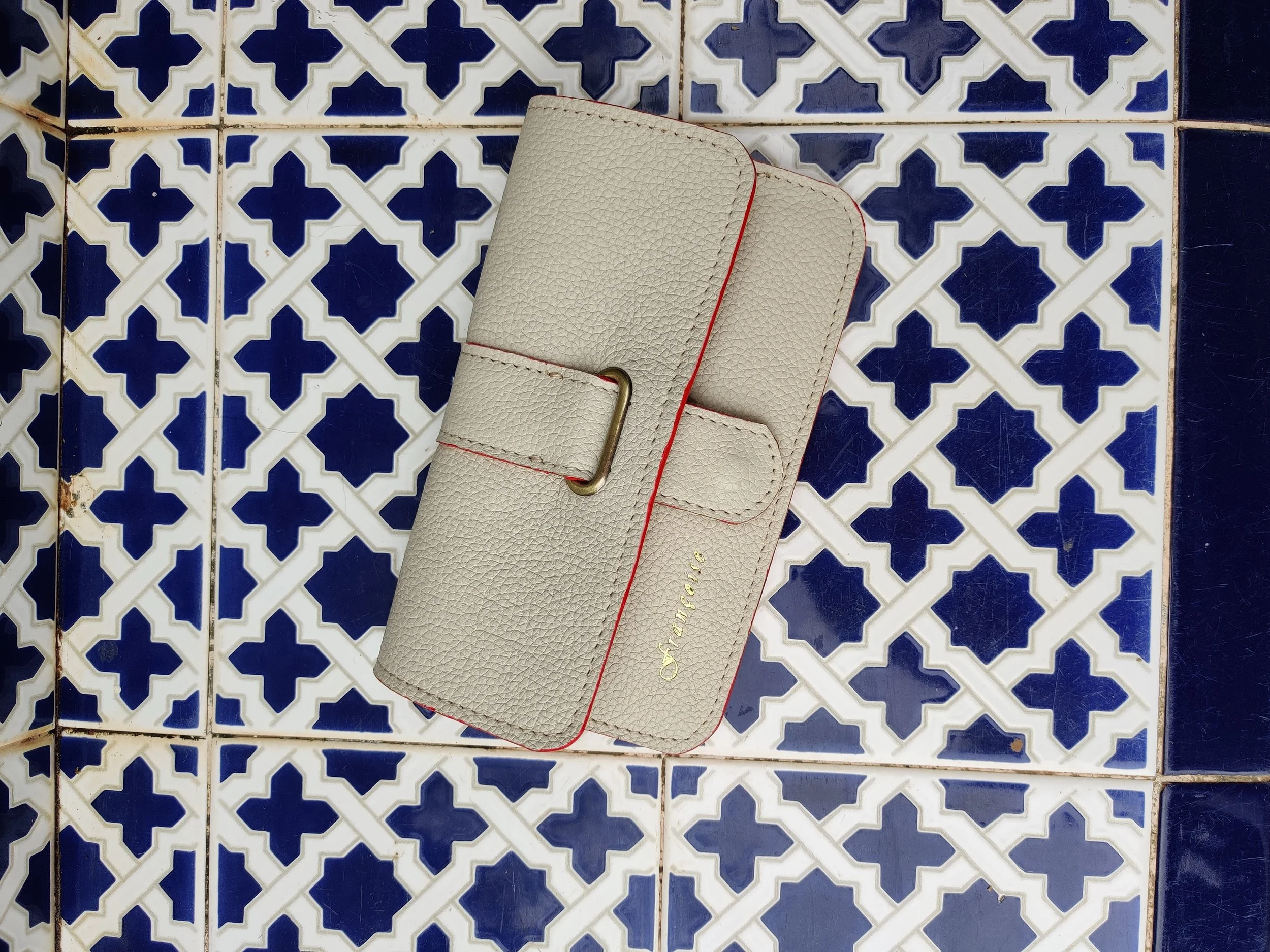 Cream-colored wallet with,lying on a patterned blue and white tiled surface.