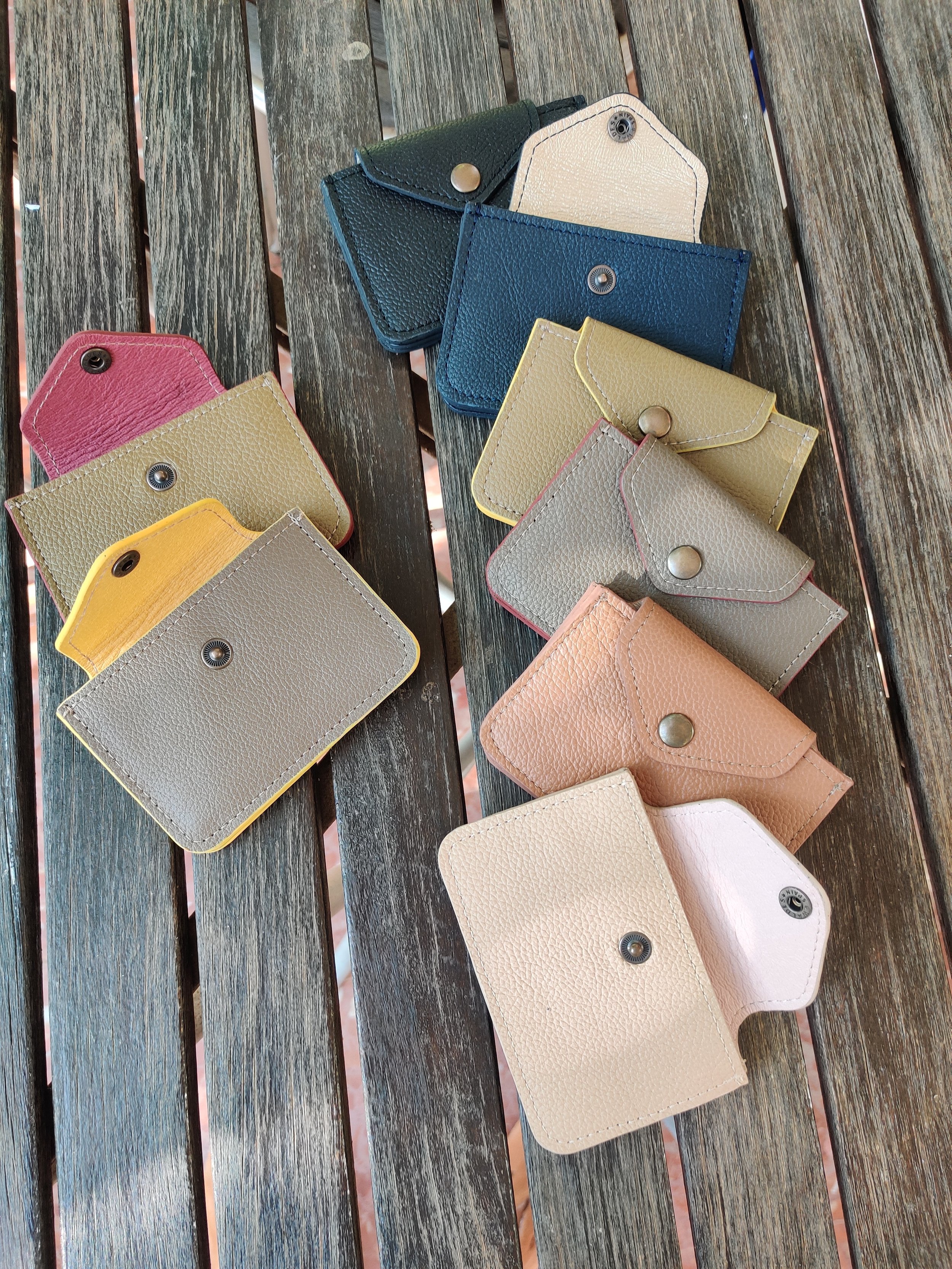 Arrangement of leather cardholders. The cardholders close with a pushbutton and are arranged on a wooden surface.