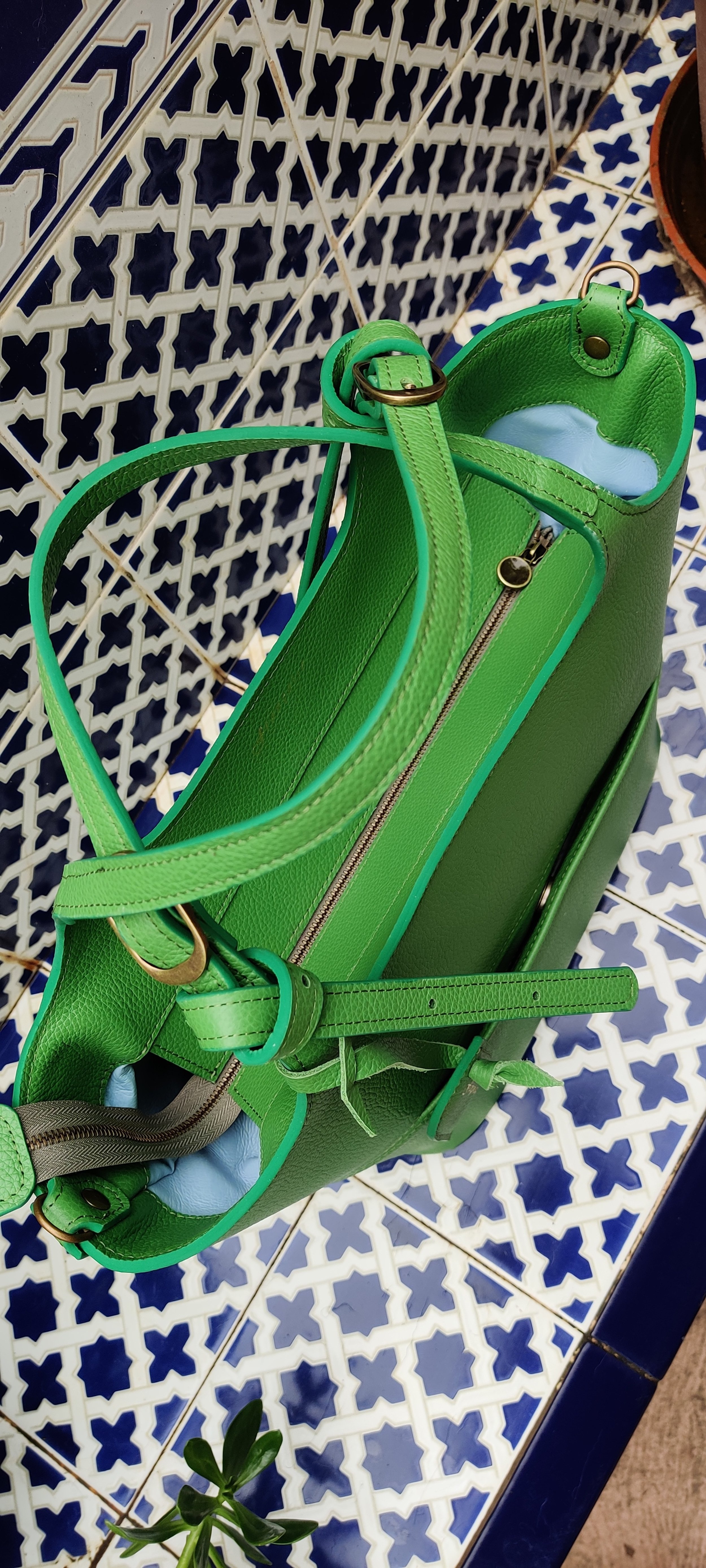 A bright green Francoise Choco Late leather handbag with a zipper, placed on a decorative blue and white tiled floor next to a potted plant.
