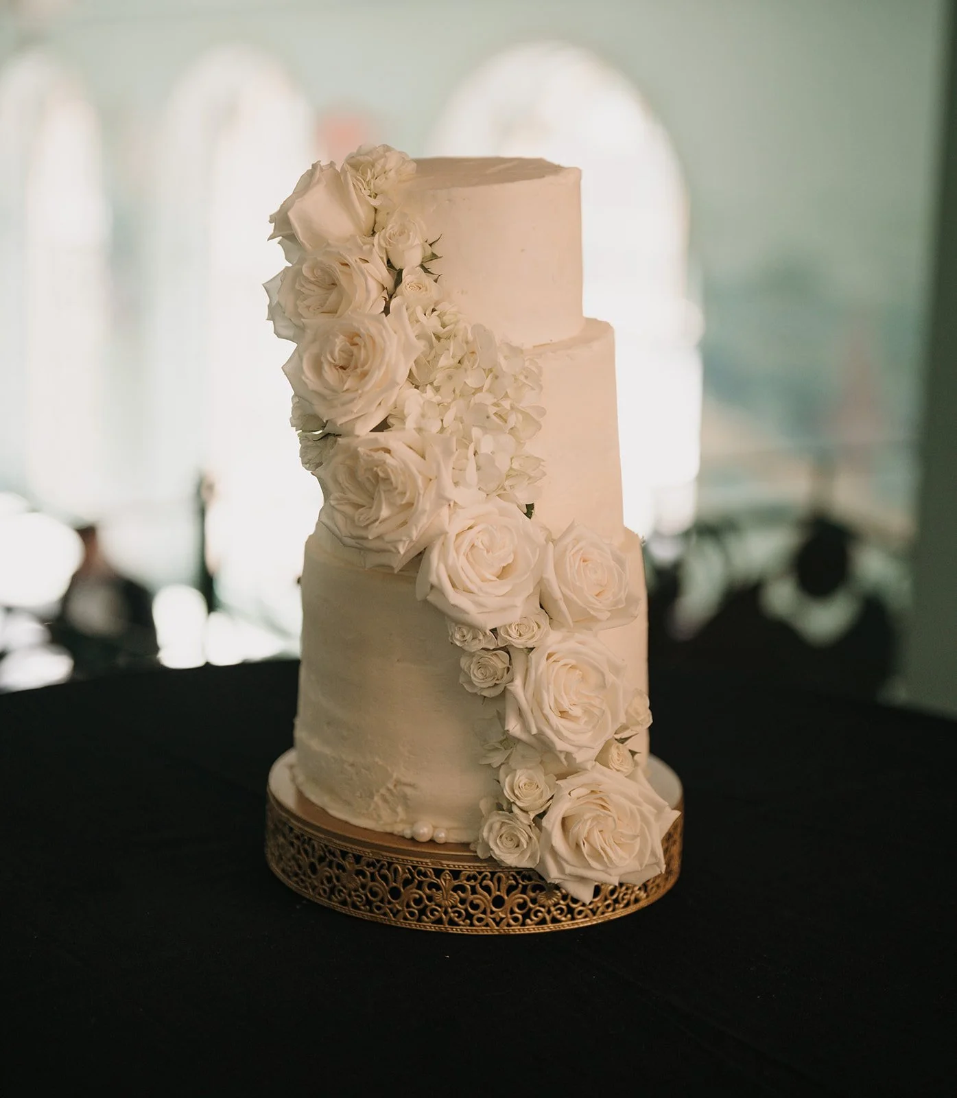 A three-tiered white wedding cake decorated with cascading white roses.