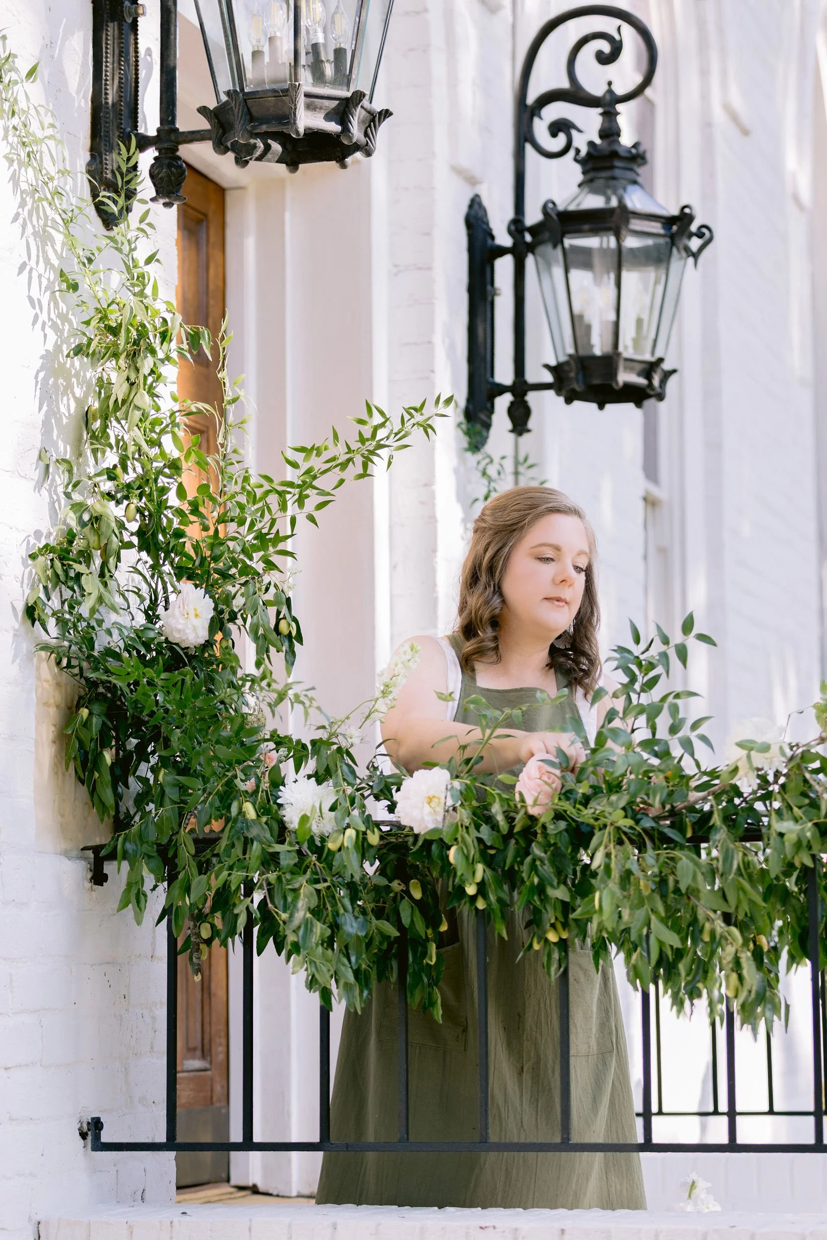 a florist decorating a black iron railing at the entrance to a white church with brown wooden door