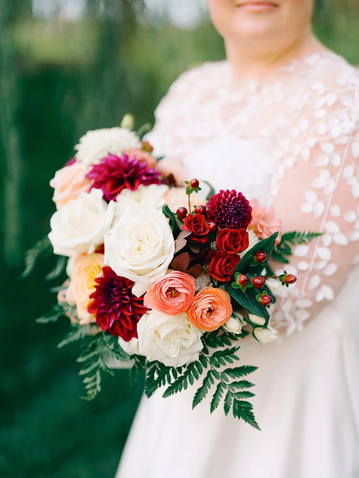 A person in a white dress holding a bouquet of various colorful flowers including roses, dahlias, and greenery in an outdoor setting.