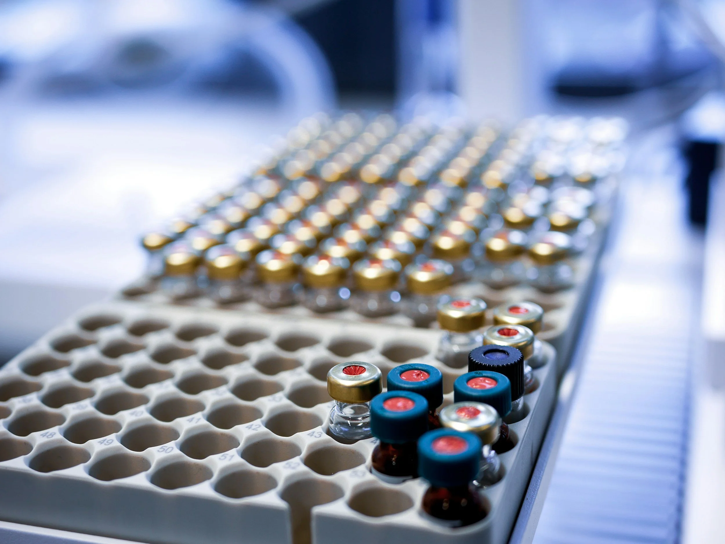 Tray of small vials with colored caps and a rack with empty labeled slots being prepared for laboratory testing.