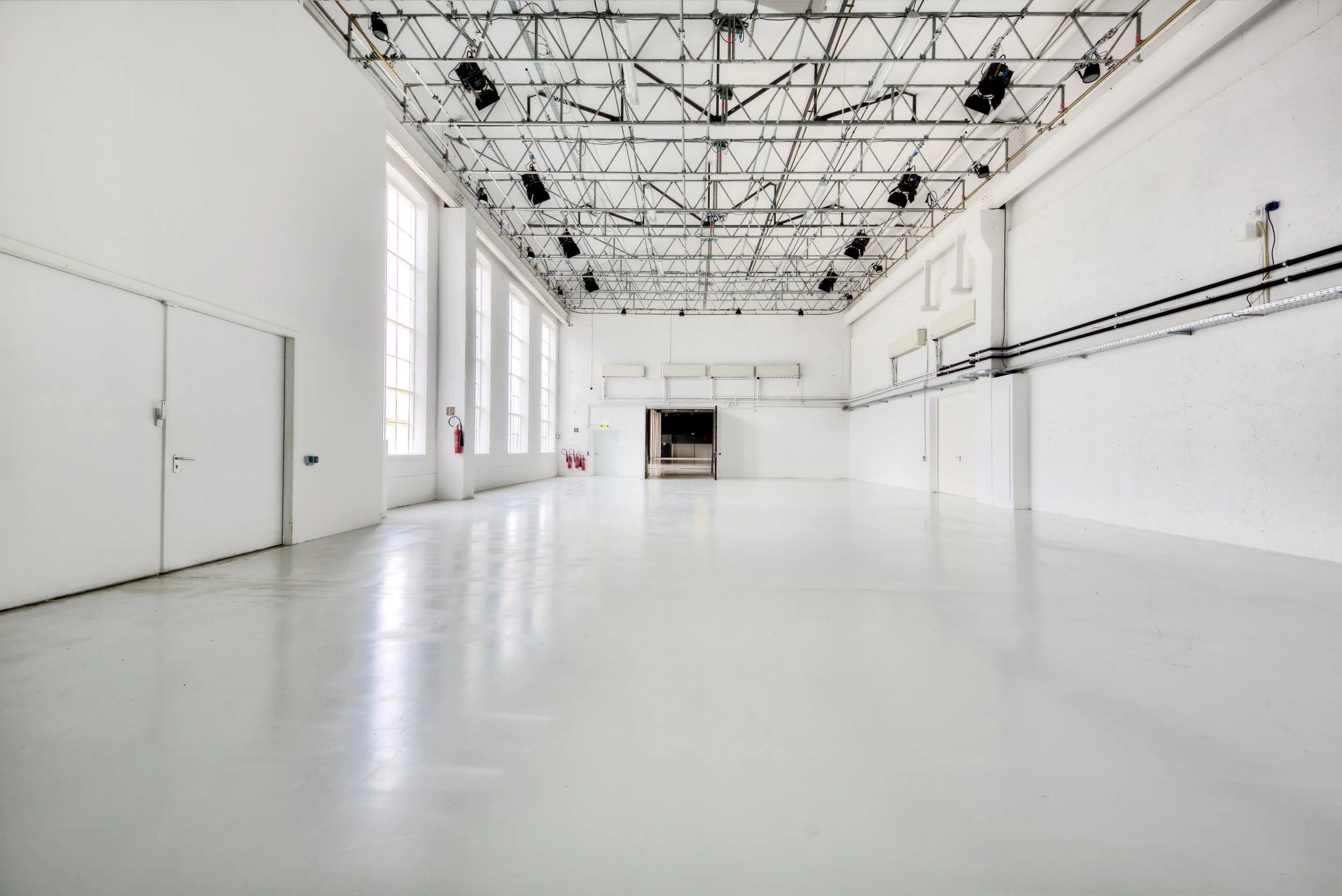 Leeres, weißes Raum mit hohen Fenstern, Studio-Decke, schwarzen Scheinwerfern, weißen Wänden und glattem Boden.