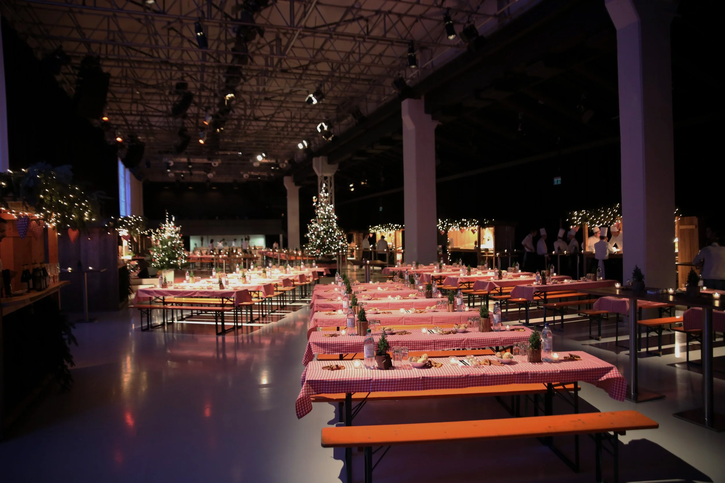 Weihnachtlich dekorierter Saal mit festlich gedeckten Tischen, Weihnachtsbäumen und Lichterketten.
