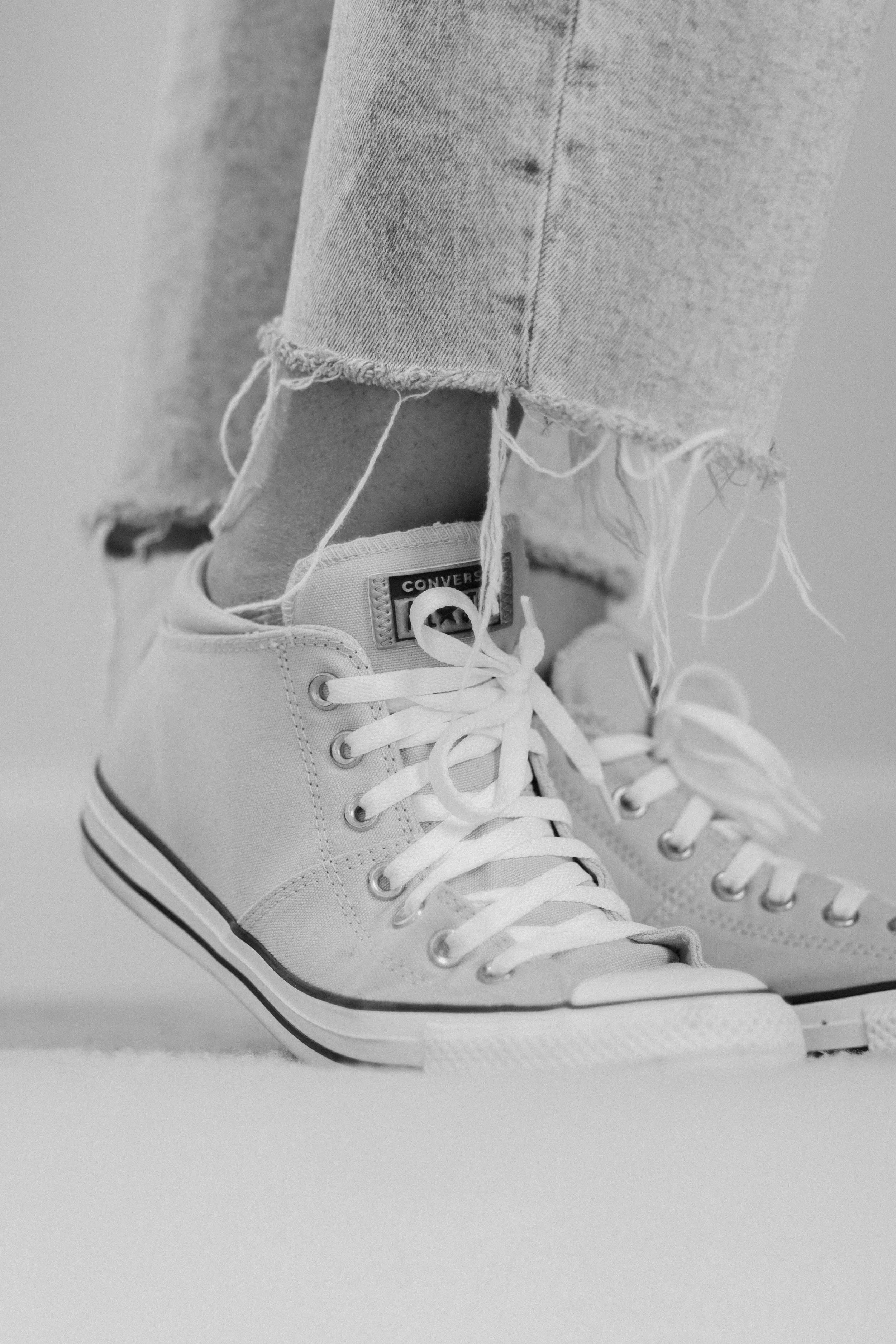 Close-up of a person's feet wearing white Converse sneakers with frayed jeans.