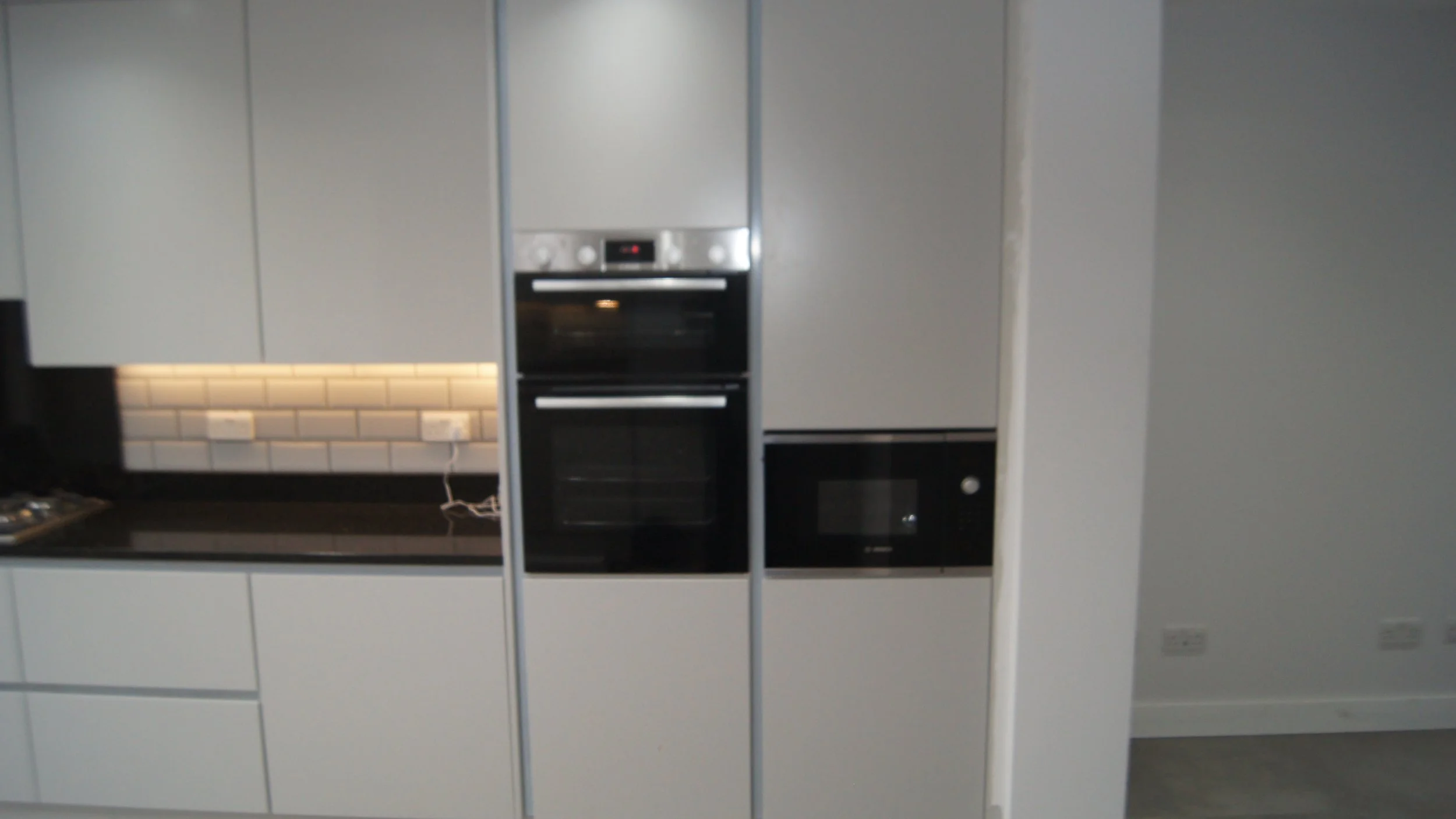 Modern kitchen with built-in oven and microwave, white cabinets, black countertop, and white subway tile backsplash.