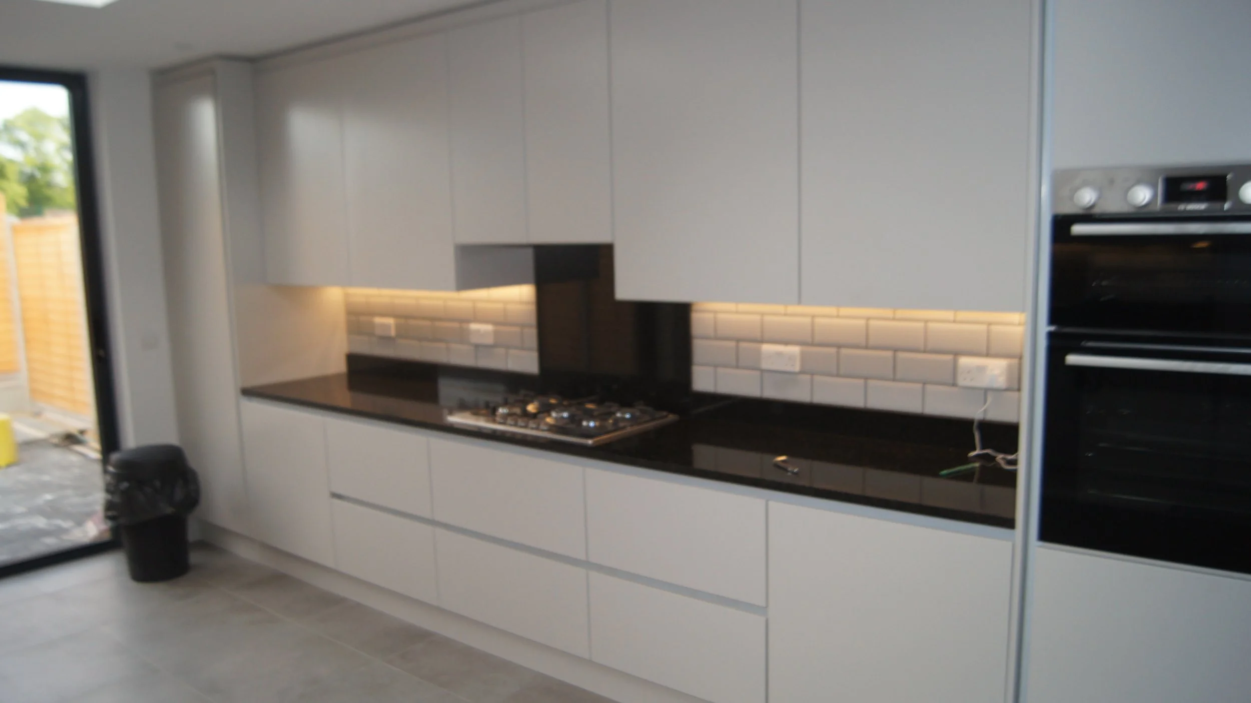 Modern kitchen with white cabinets, black countertop, white brick backsplash, and a built-in oven.