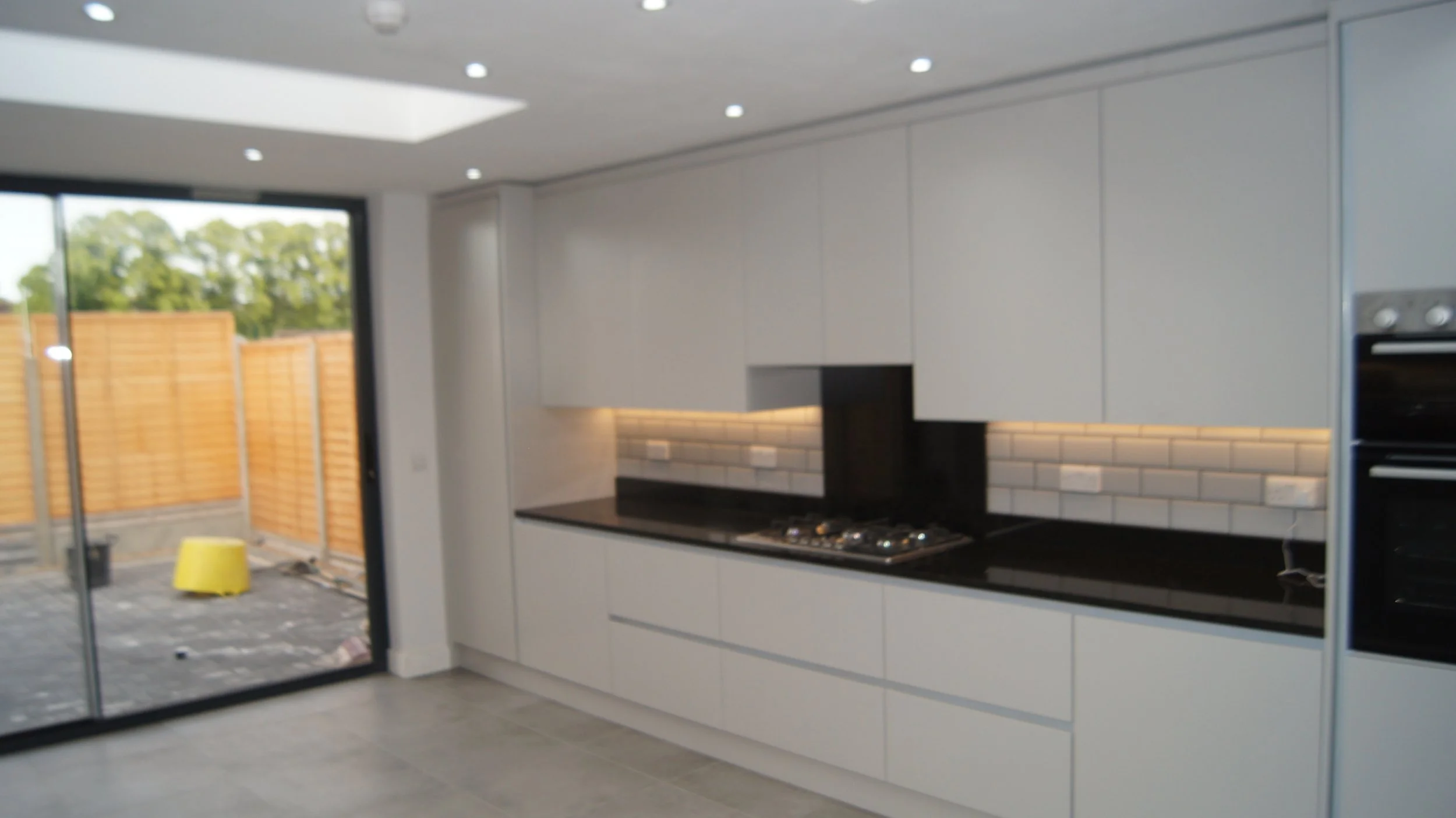 Modern kitchen with white cabinets, black countertops, and a brick tile backsplash, adjacent to a sliding glass door leading to an outdoor patio.